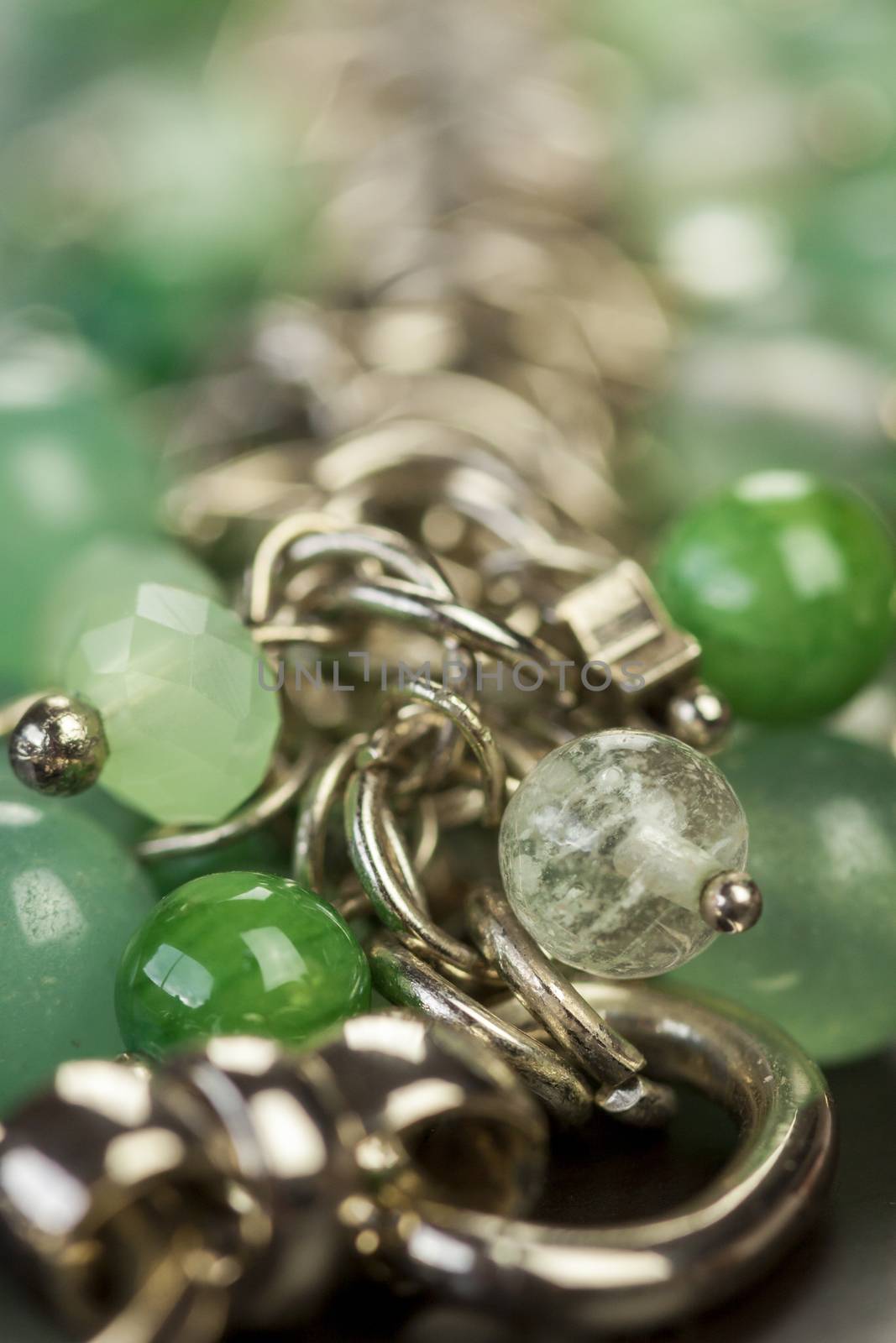 Close up view of pretty translucent green beads on an item of silver jewellery attached in a bunch to a ring by short chains with shallow dof in a fashion concept