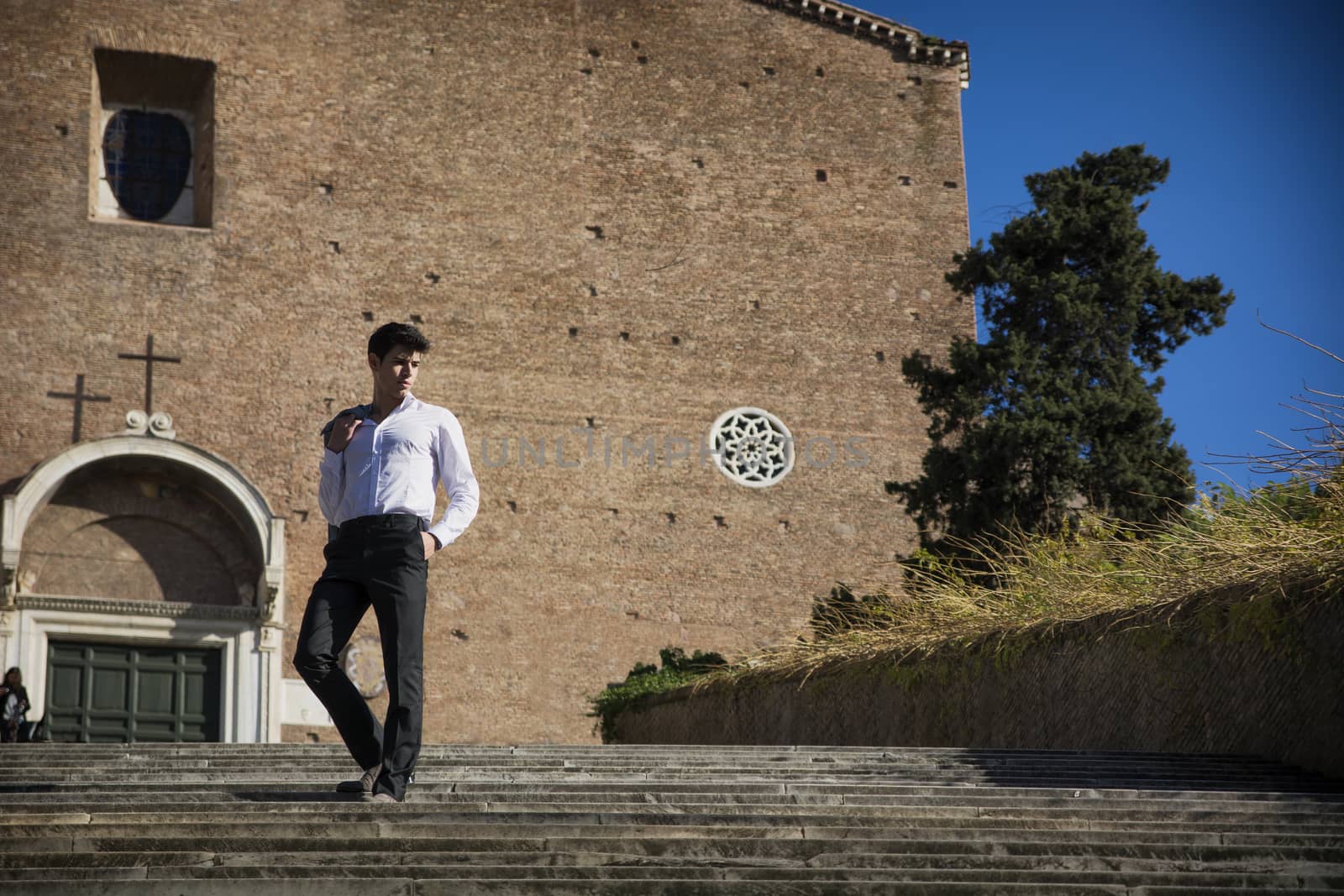 Young man walking down old stair in front of church in Rome, Italy by artofphoto