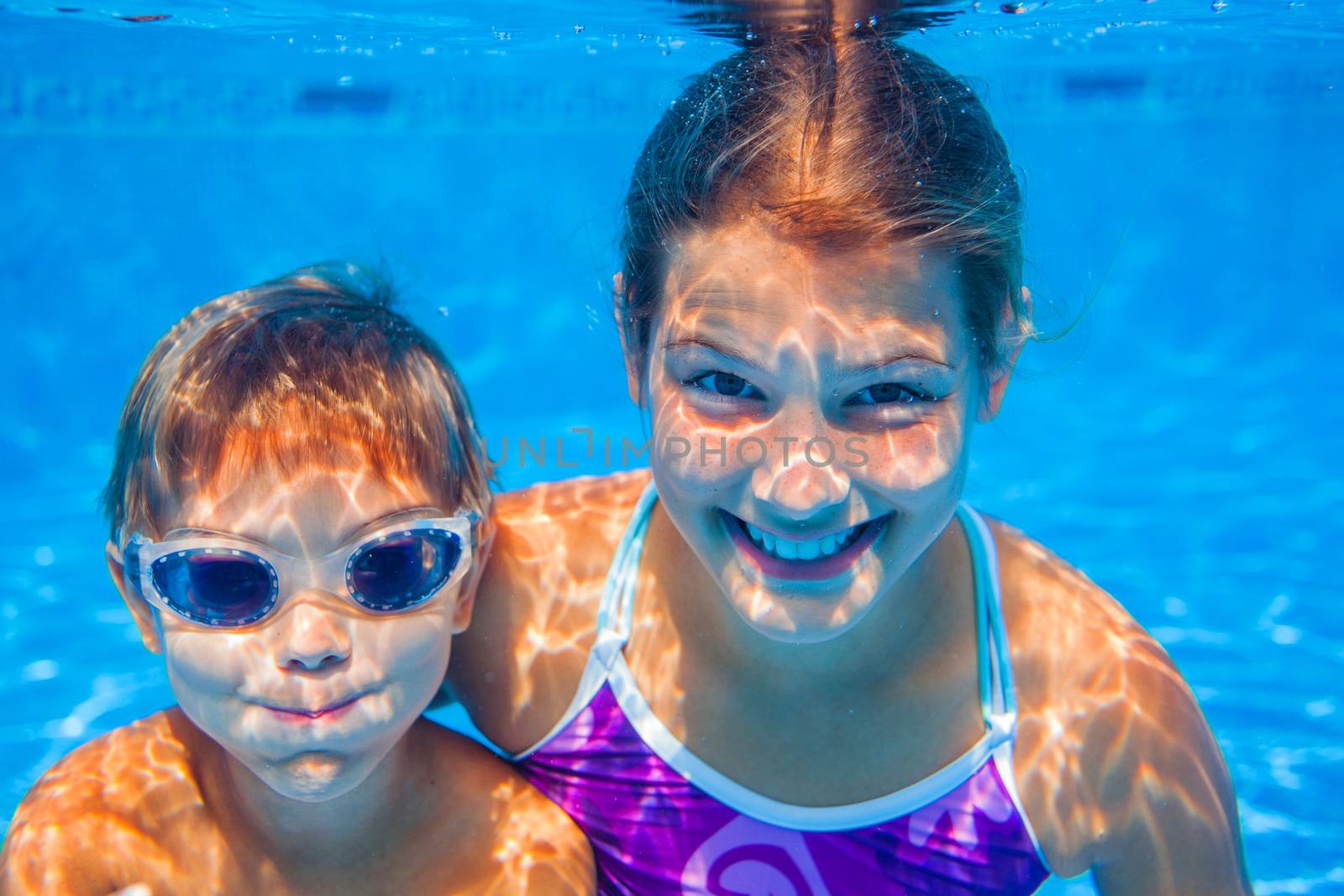 Underwater happy cute girl and boy in swimming pool