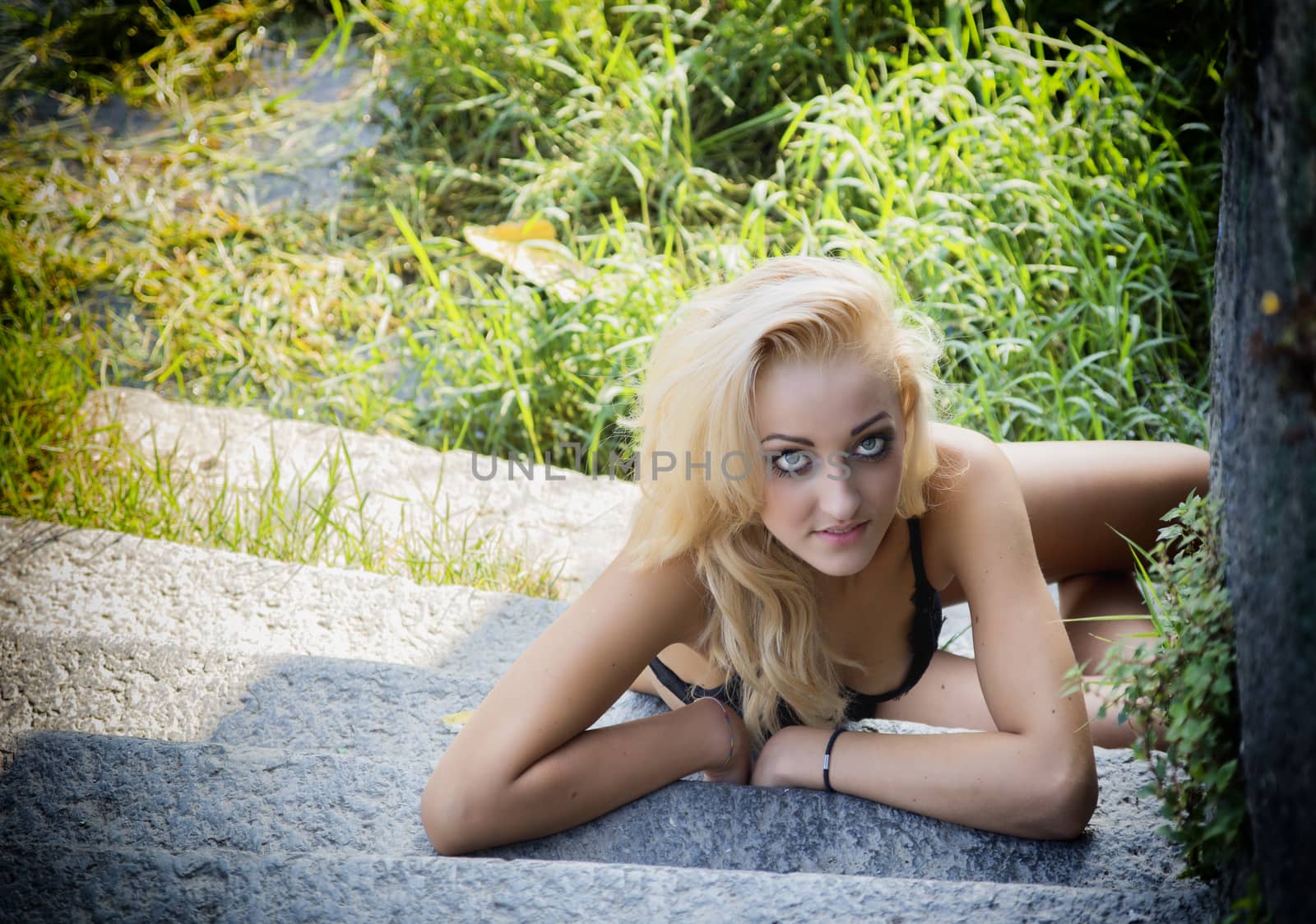 Pretty blonde young woman outdoor laying on stone stairs looking up at camera