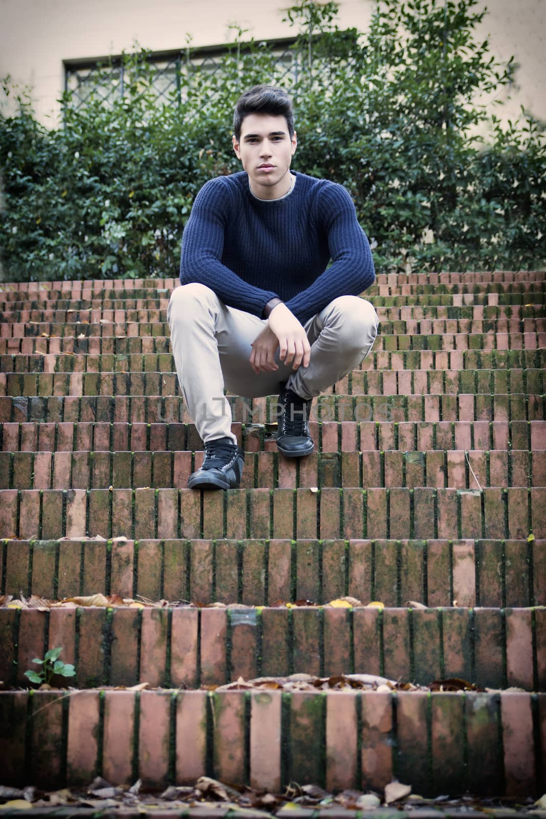 Handsome young man sitting outdoor on old brick stairs looking confident at camera