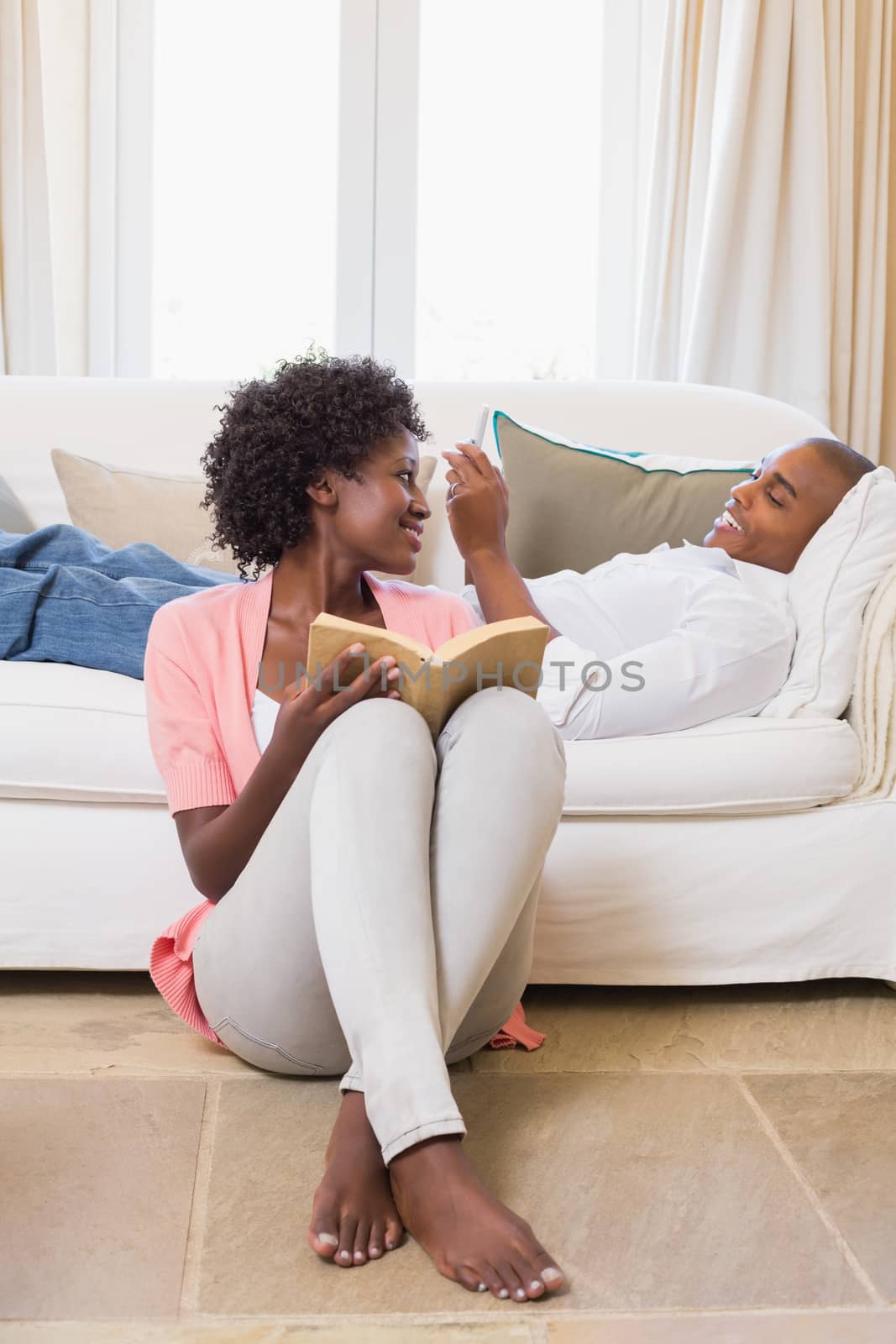 Cute couple relaxing reading book and using smartphone at home in the living room