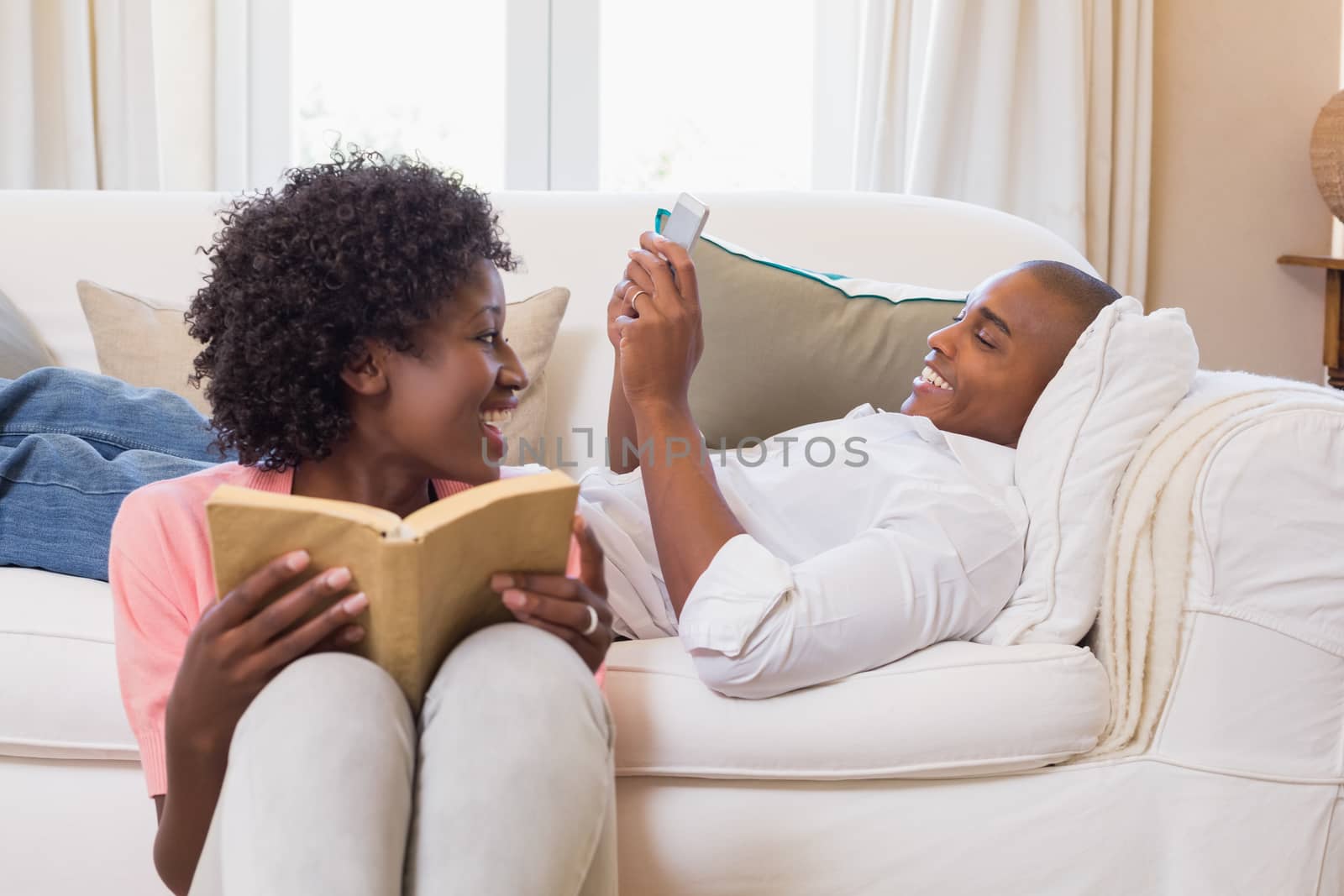 Cute couple relaxing reading book and using smartphone at home in the living room