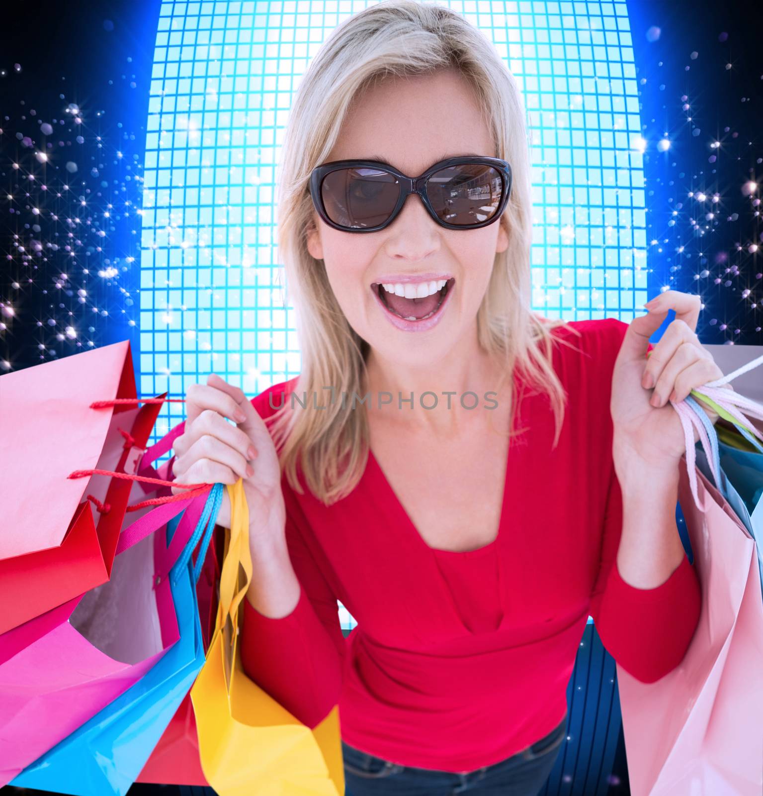 Happy blonde holding shopping bags against glittering screen on black background