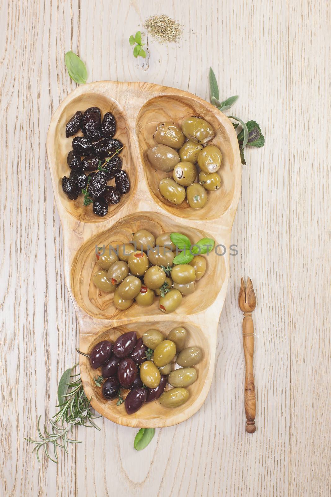 Variety of green, black and mixed marinated olives in olive tree dish on wooden table