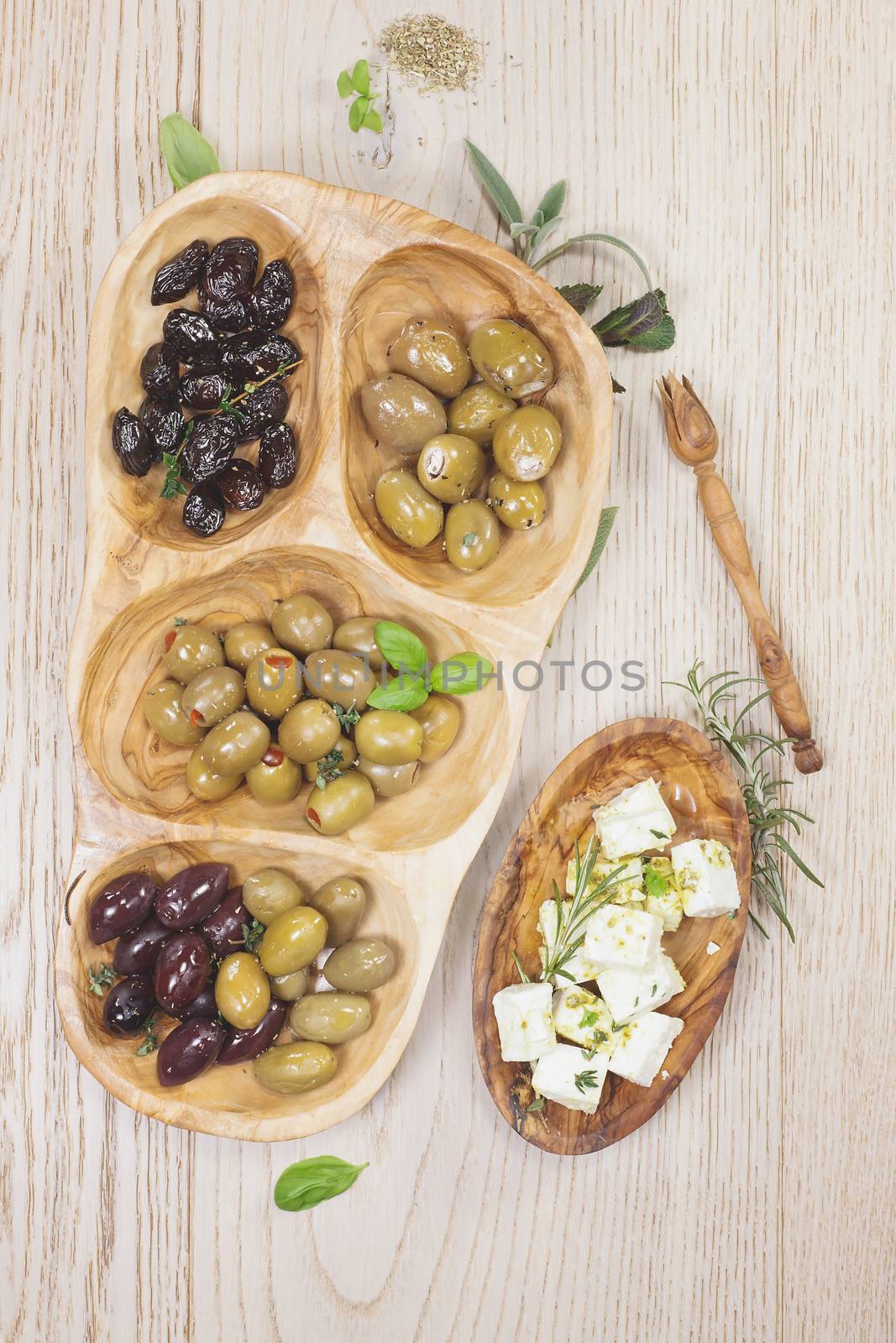 Assorted olives and feta or goat cheese cheese in olive tree dish on wooden table