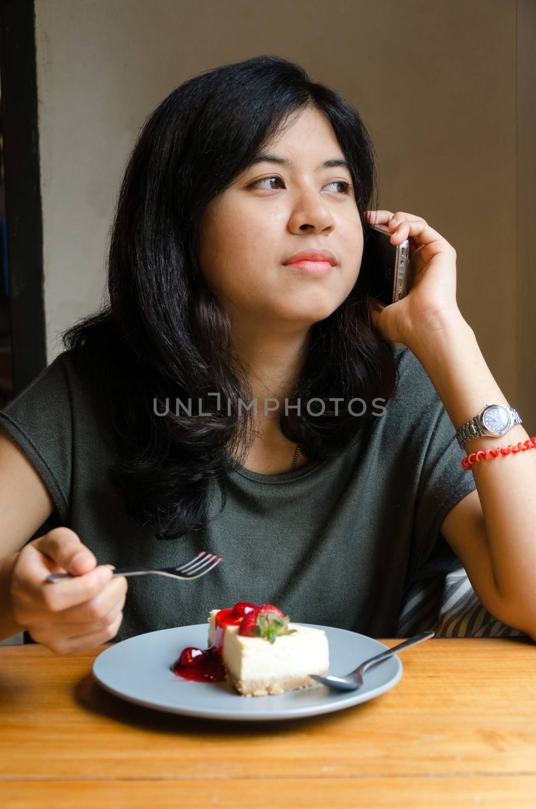 Young asian woman talking mobile phone with a cake in cafe