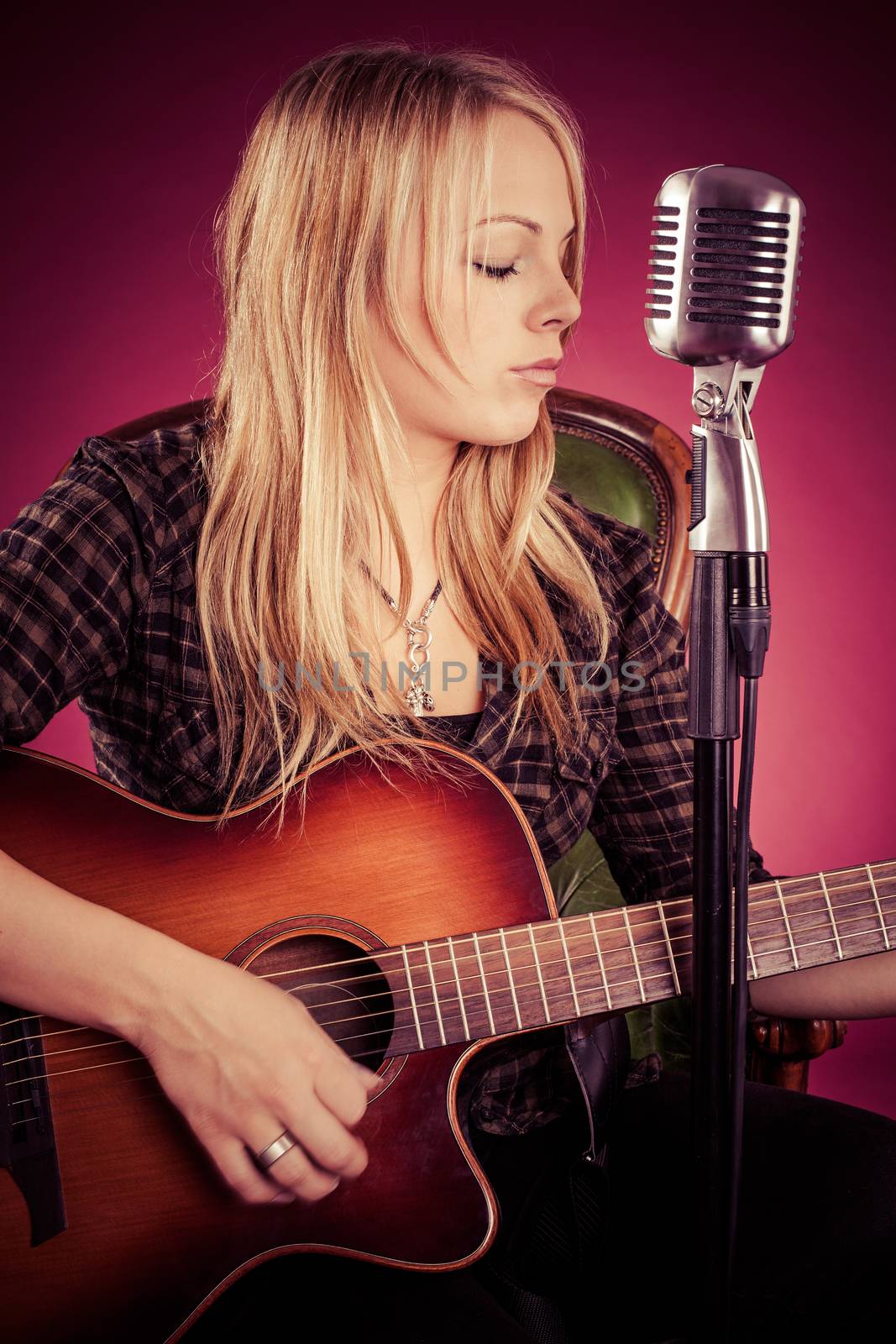 Photo of a beautiful blond woman playing an acoustic guitar. Filtered to have a vintage look.