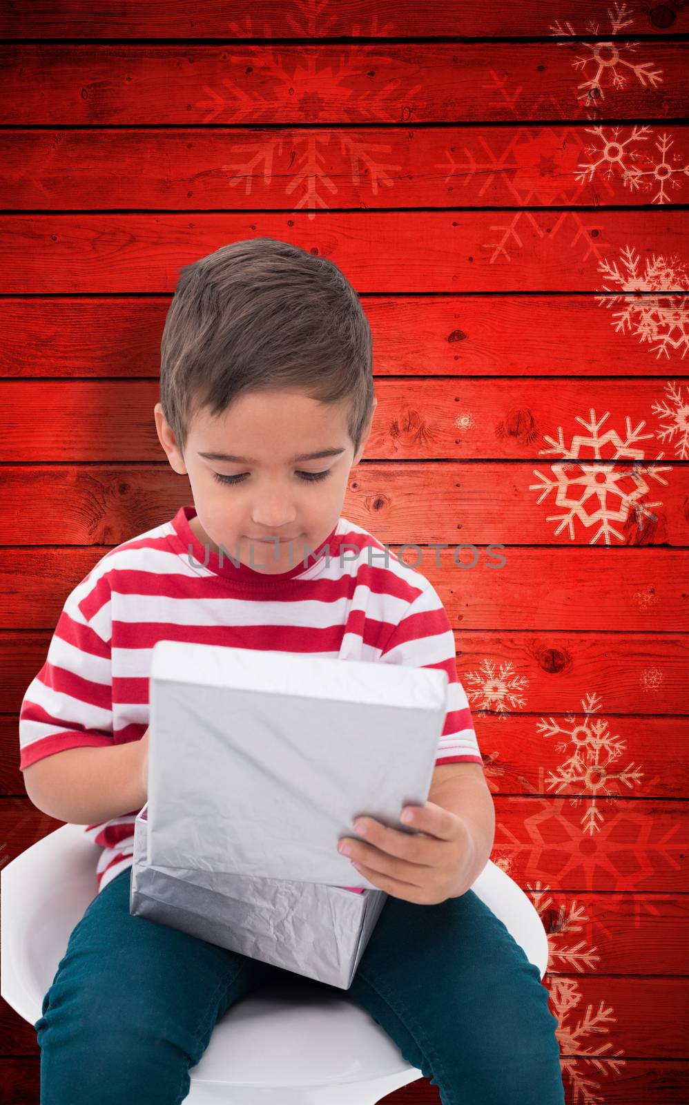 Cute little boy opening gift against snowflake pattern on red planks