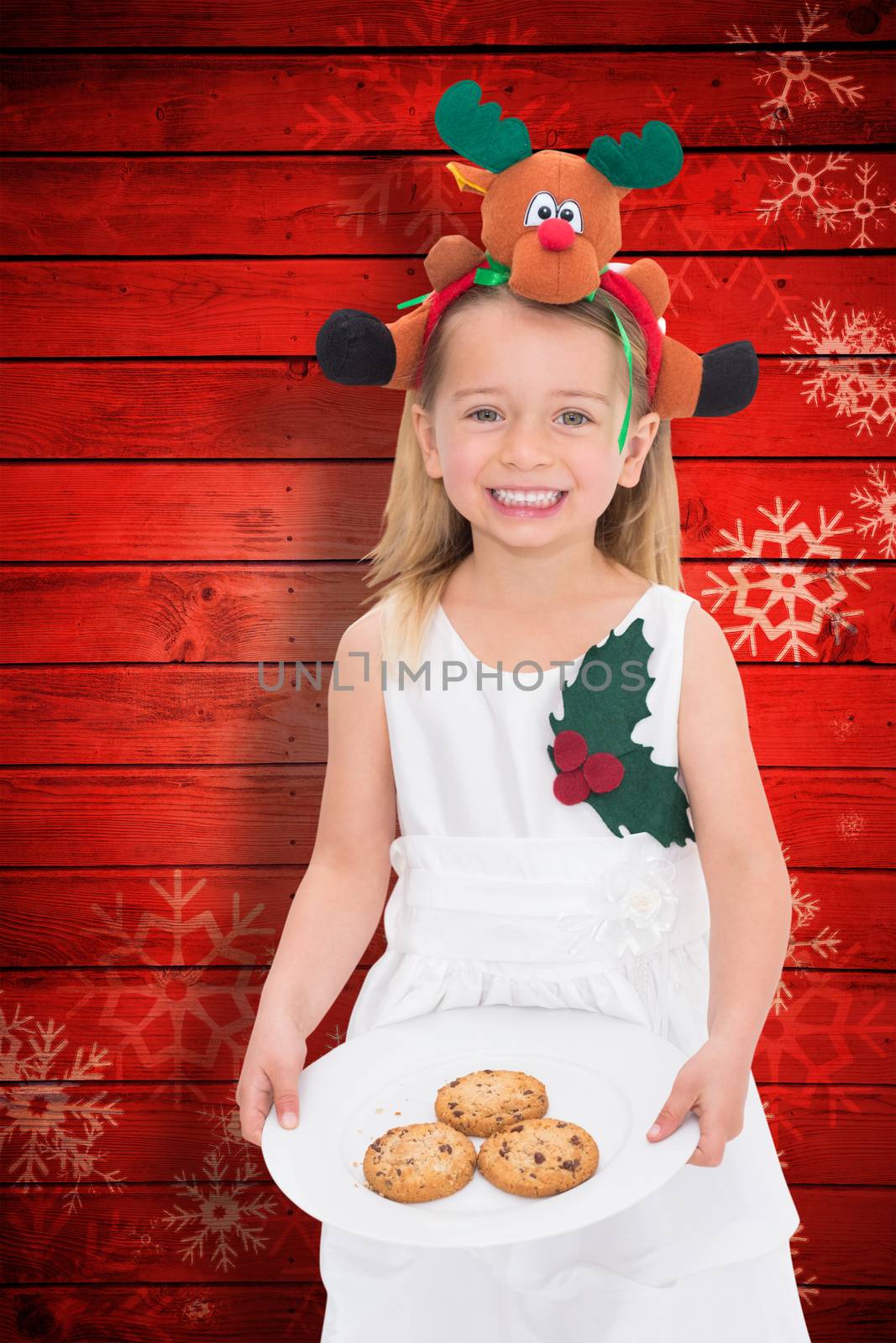 Festive little girl holding fresh cookies against snowflake pattern on red planks