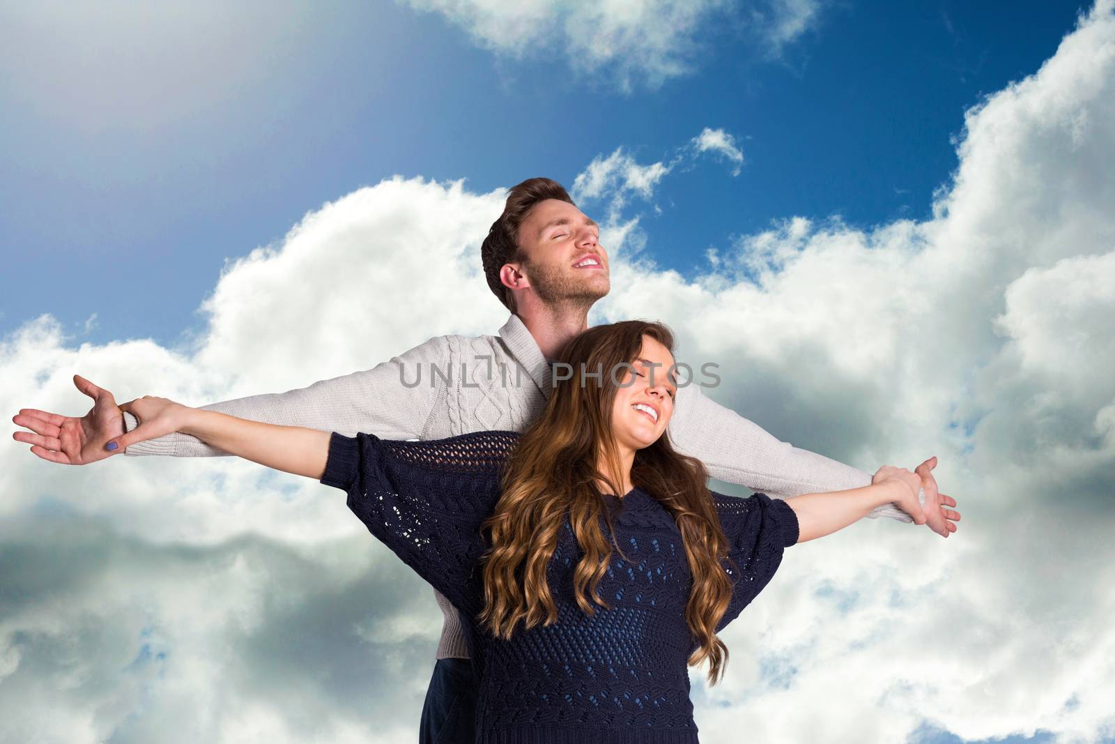 Romantic young couple with arms out against blue sky with clouds
