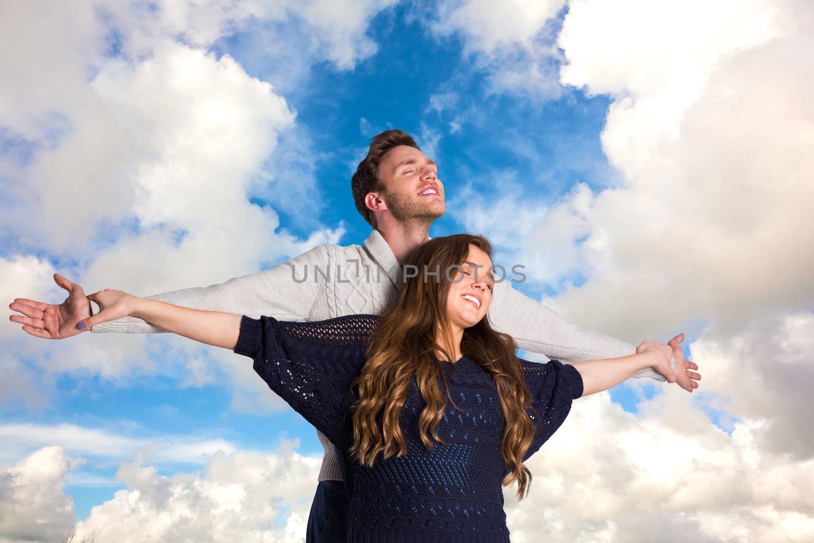 Romantic young couple with arms out against blue sky with white clouds
