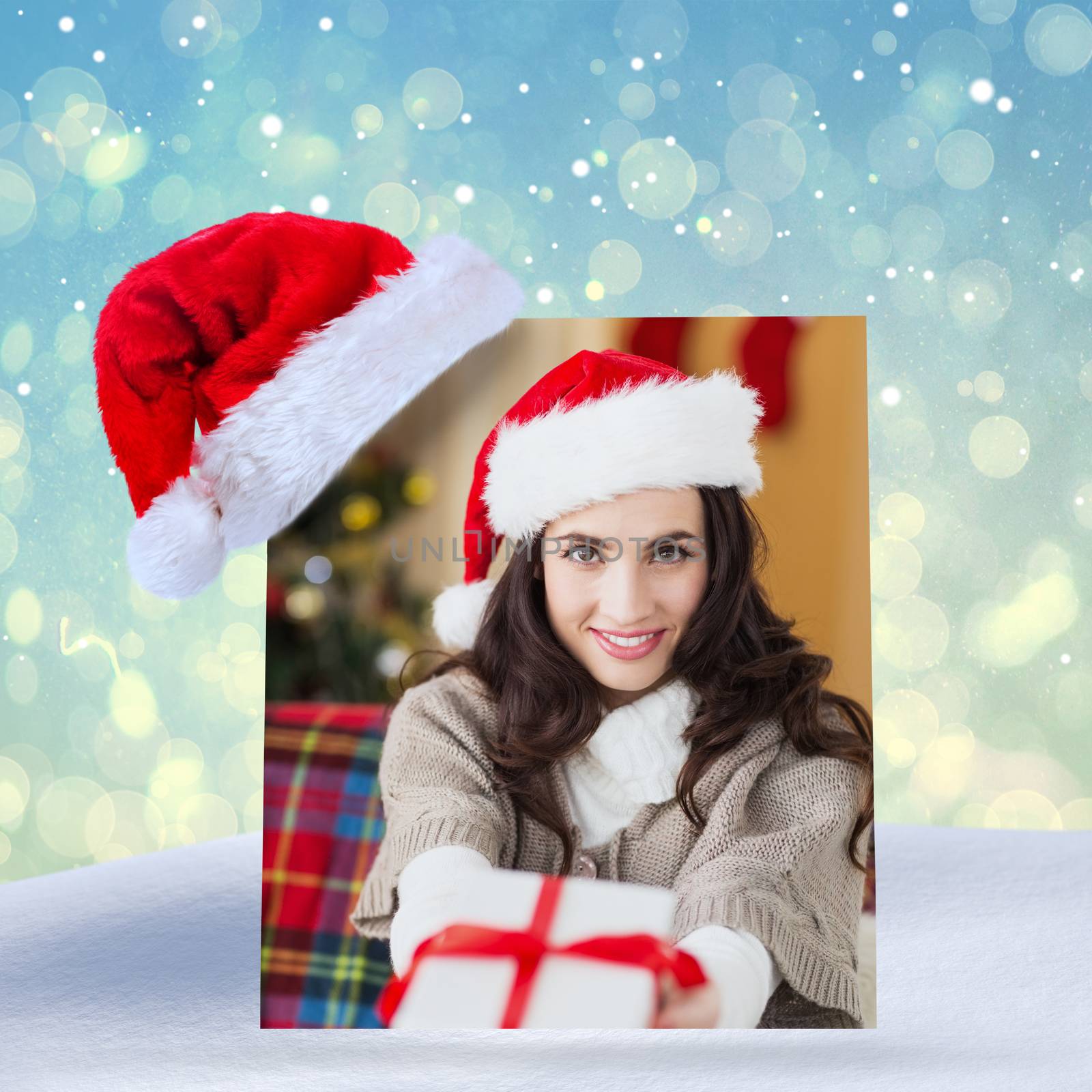 Festive brunette showing gift at christmas against blue abstract light spot design