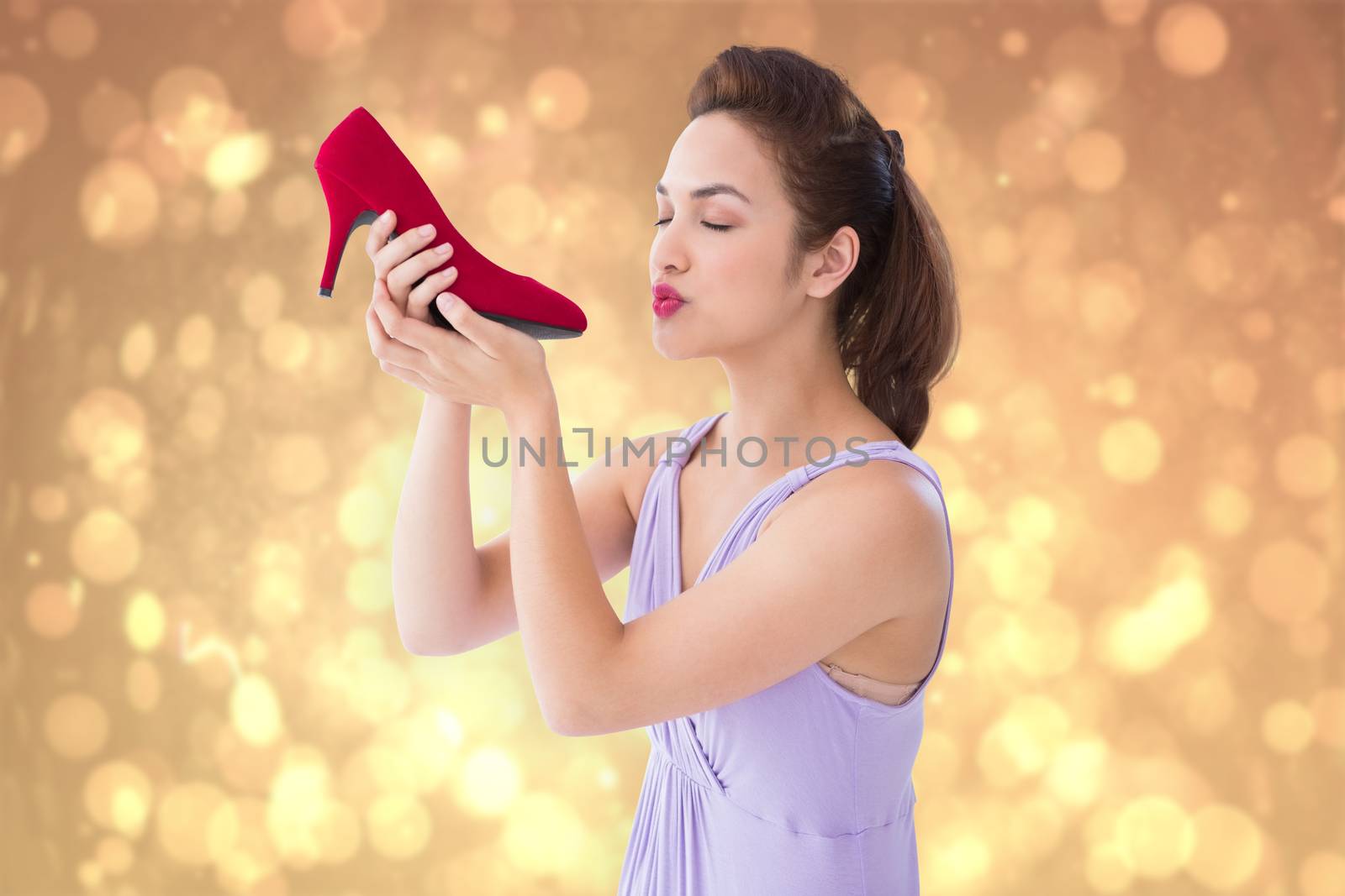 Elegant brunette kissing a shoe  against yellow abstract light spot design