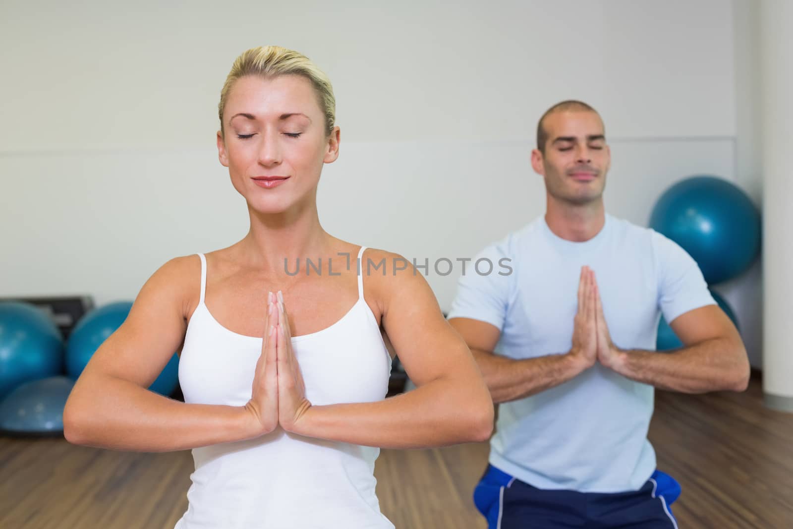 Sporty young couple with joined hands and eyes closed at fitness studio
