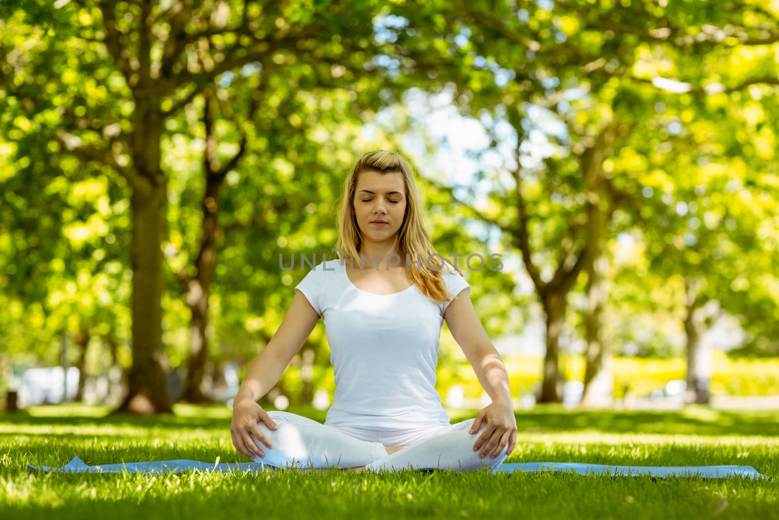 Fit blonde sitting in lotus pose in the park on a sunny day