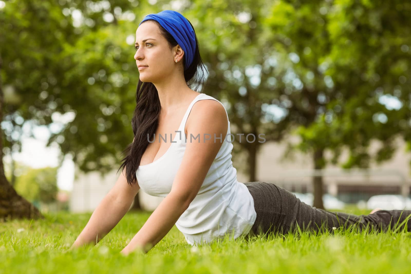 Smiling brunette doing yoga on grass in the park