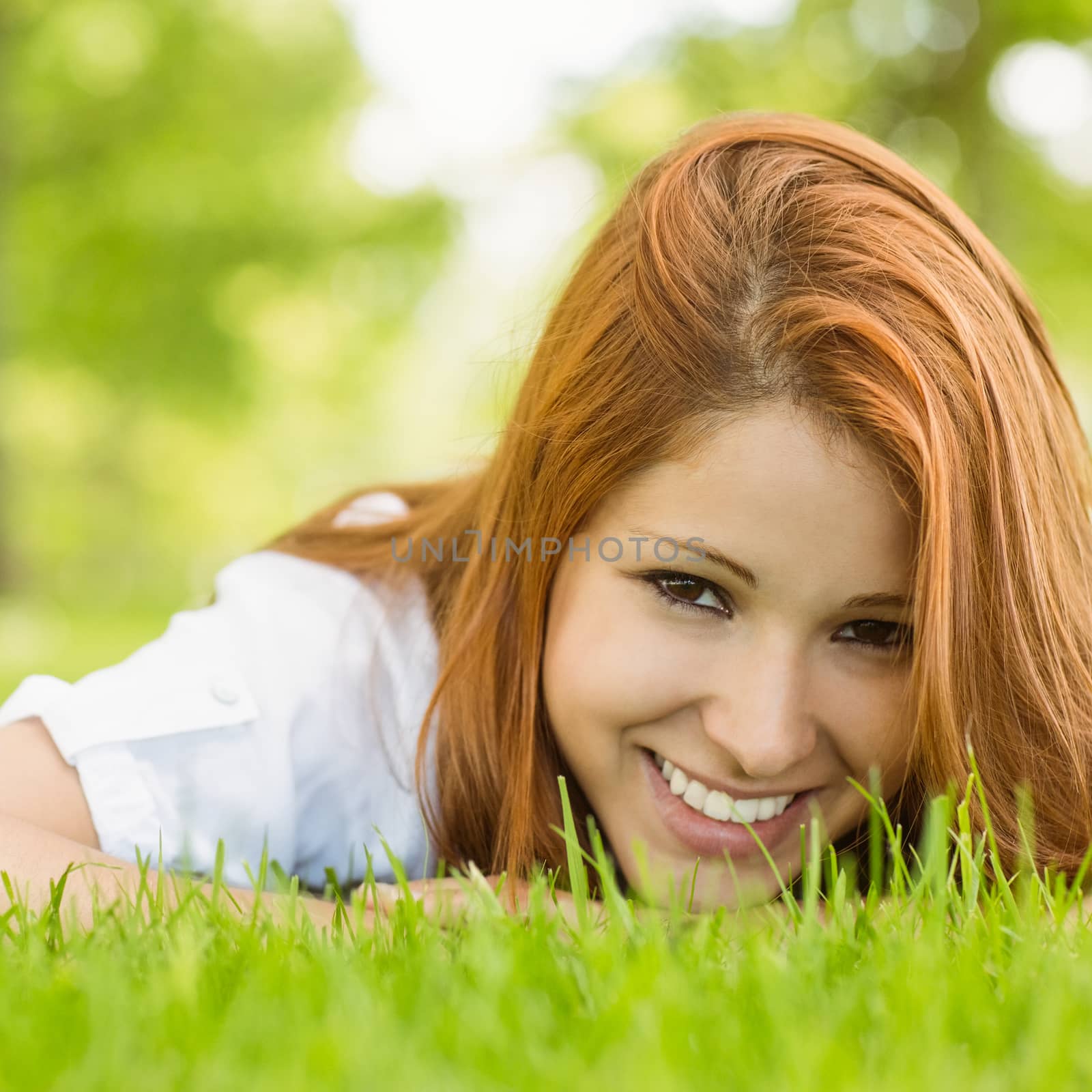 Portrait of a pretty redhead smiling and lying on grass in park