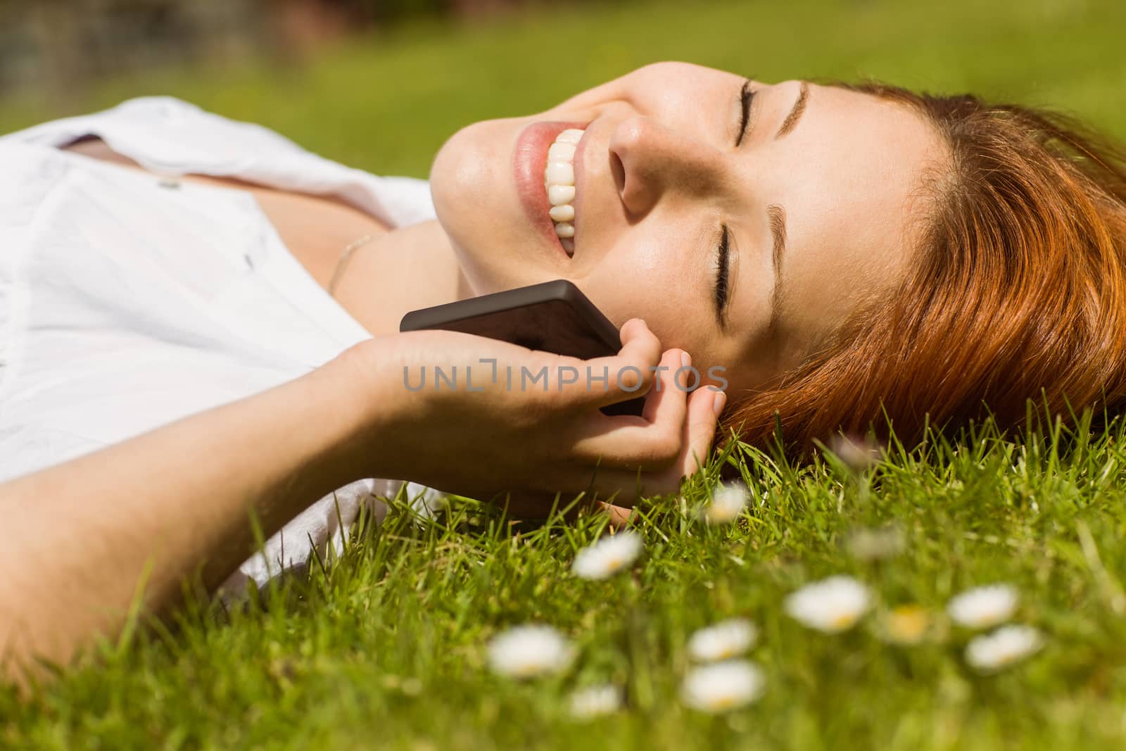 Pretty redhead calling and lying on grass at summer