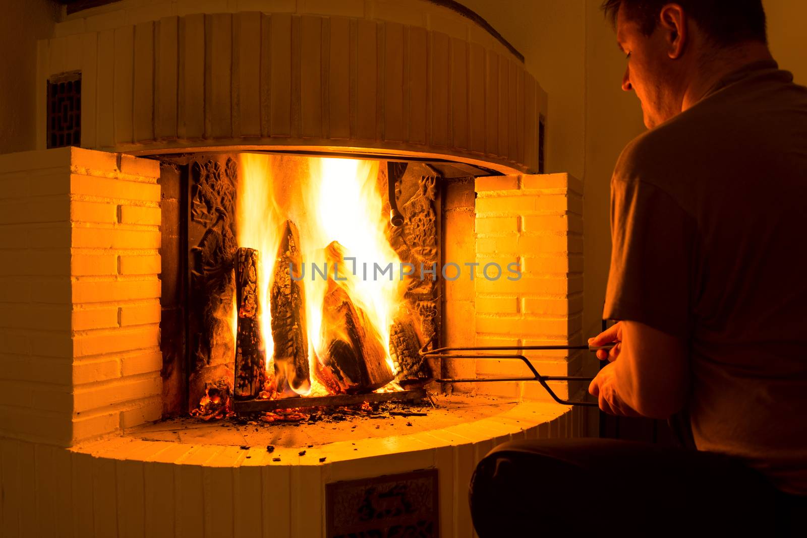 Man adjusting firewood in burning fireplace