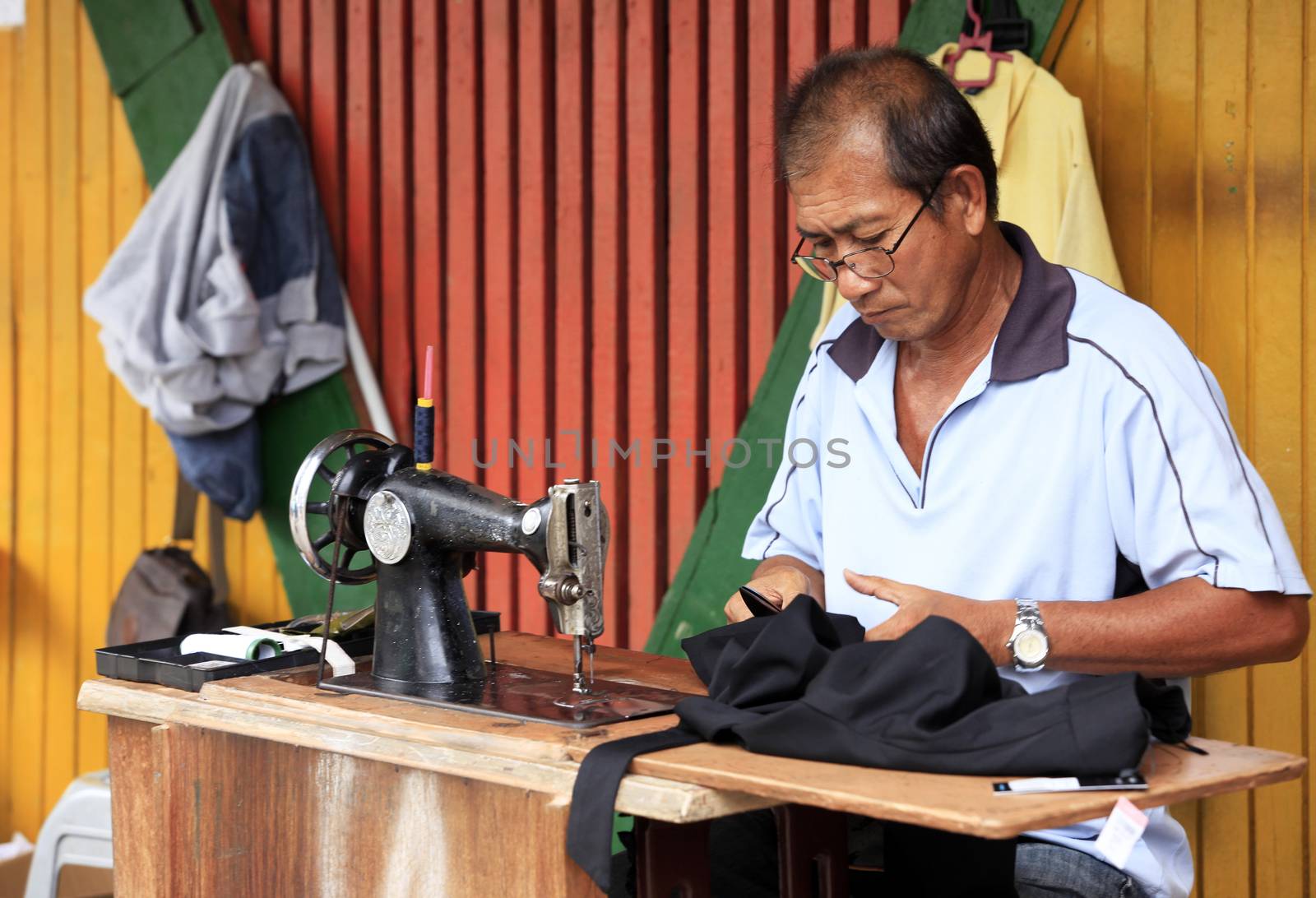 Kota Kinabalu, Malaysia-  December 31, 2014: Street tailor with his old mechanic sewing machine at work in his small shop. This kind of job is very common in Malaysia.