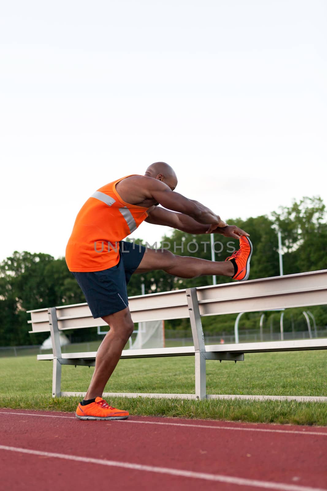 African American man in his 30s stretching at a sports track outdoors.