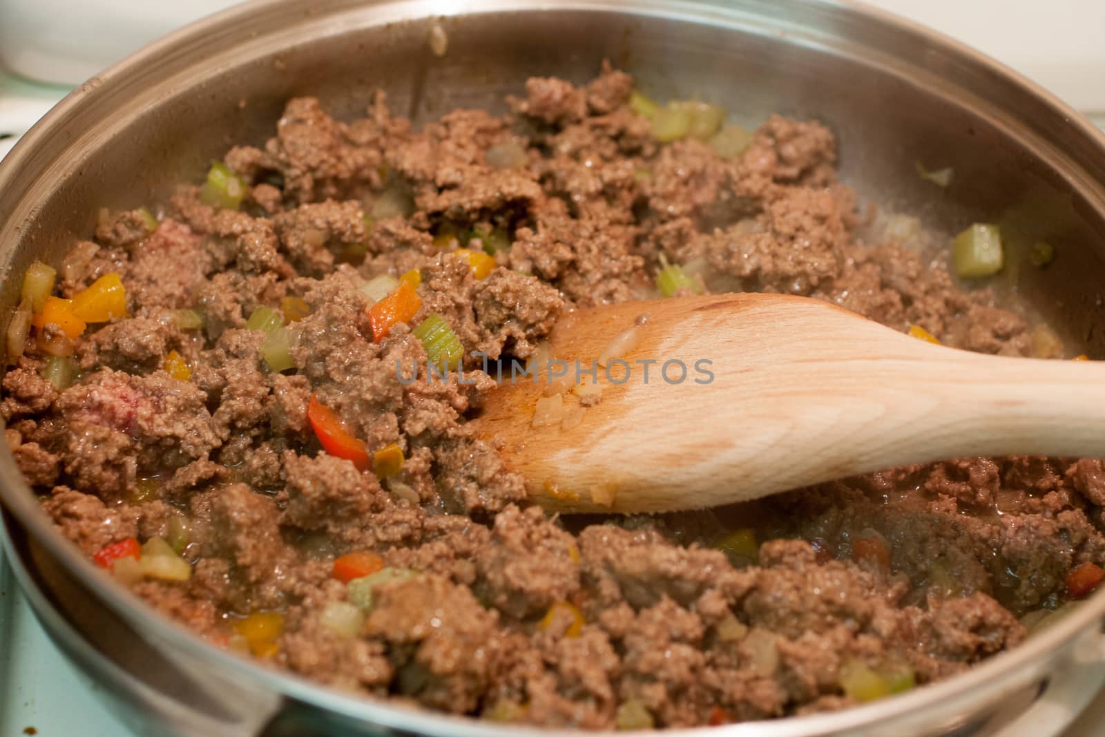 Fresh ground beef and vegetables cooking in a skillet with a wooden spoon stirring it.