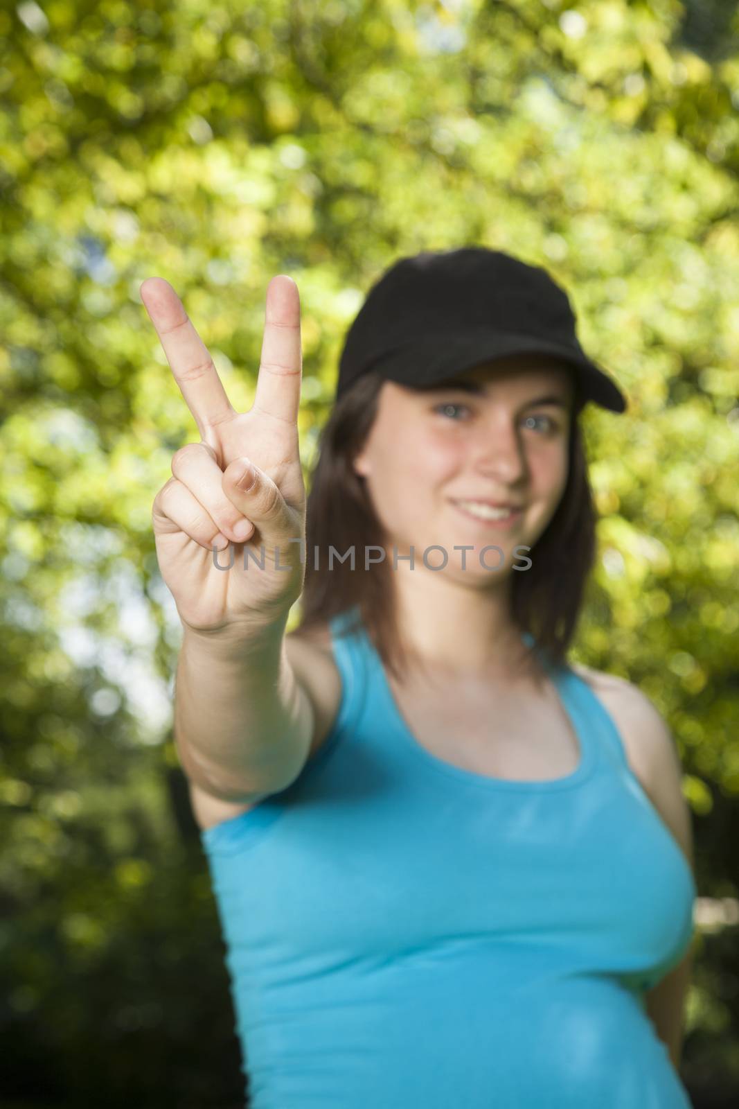 pregnant young woman with blue shirt victory hand gesture over green trees background street