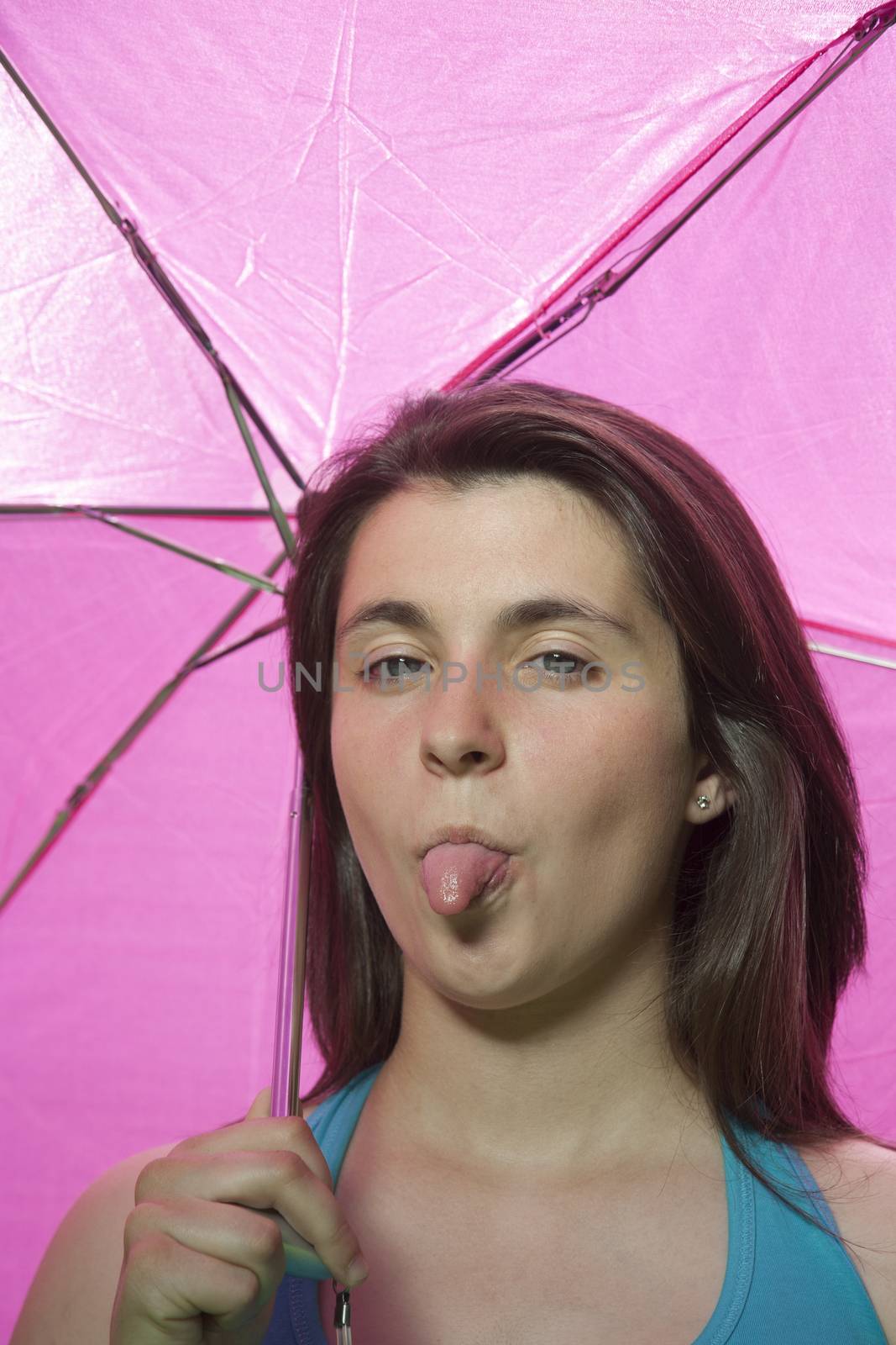 pretty young woman with blue shirt teasing sticking out tongue and pink umbrella background
