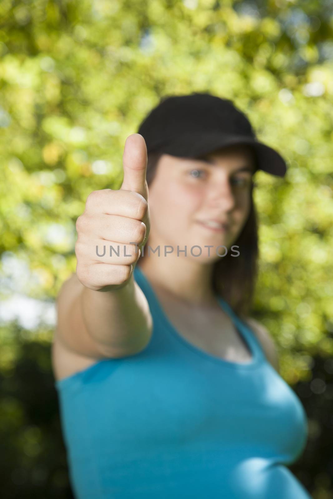 pregnant young woman with blue shirt black cap thumb up over green trees background street
