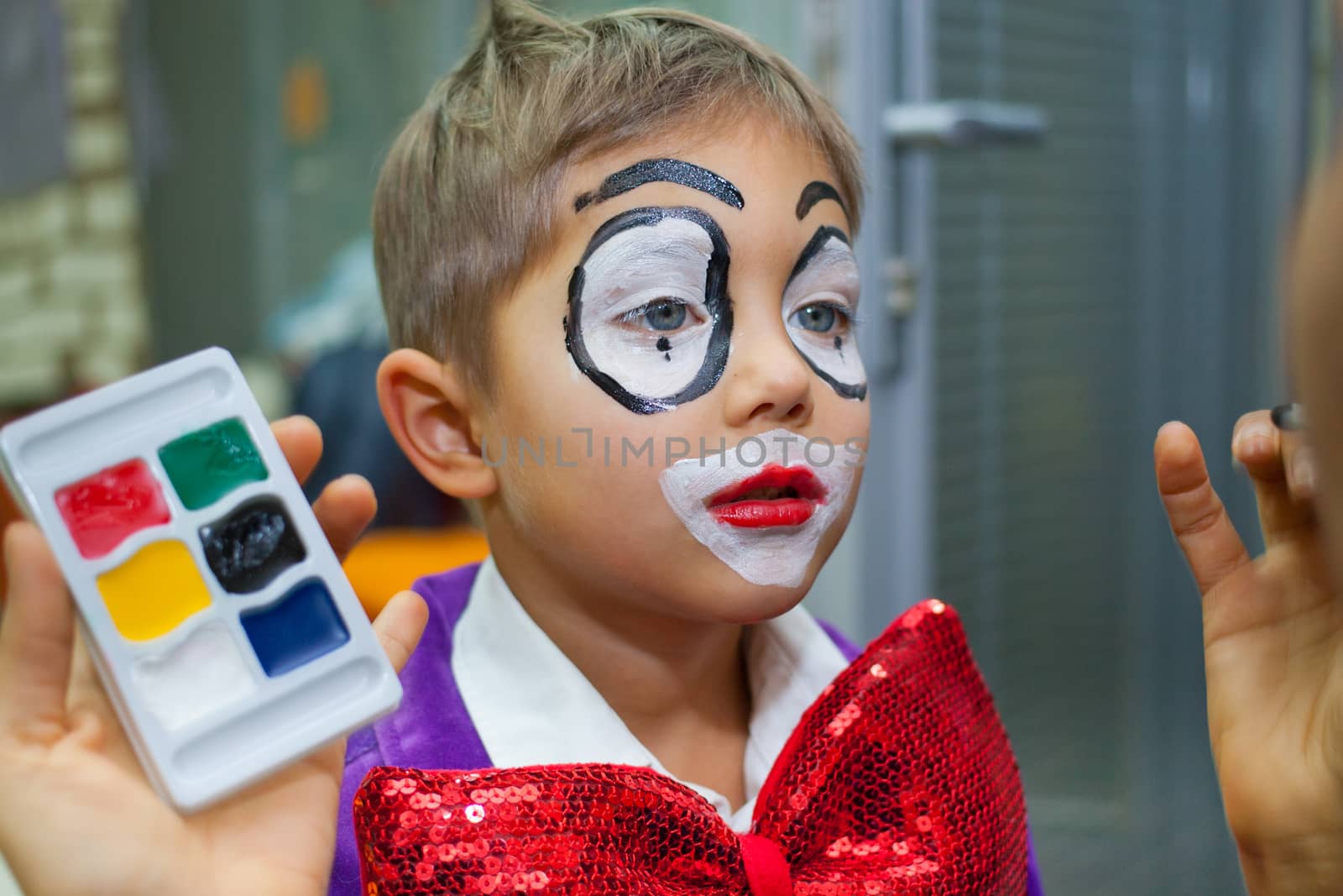 Preparing for the holiday - Clown makeup for cute little boy. 