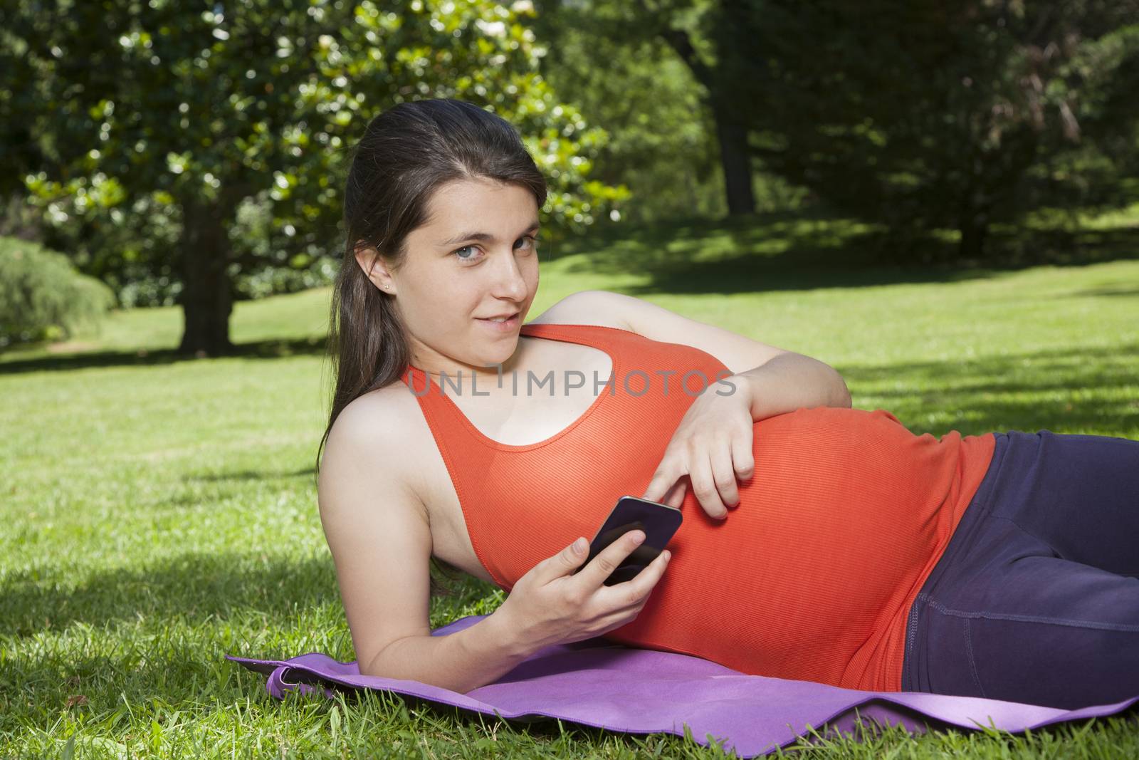 pregnant young woman with orange shirt touching smartphone at a park in Madrid Spain Europe