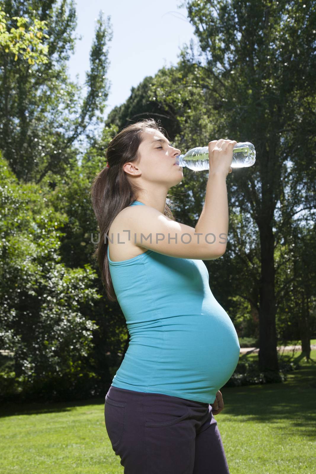 pregnant young woman with blue shirt drinking water from plastic bottle at a park in Madrid Spain Europe