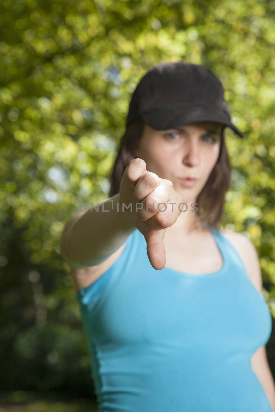 pregnant young woman with blue shirt black cap thumb down over green trees background street