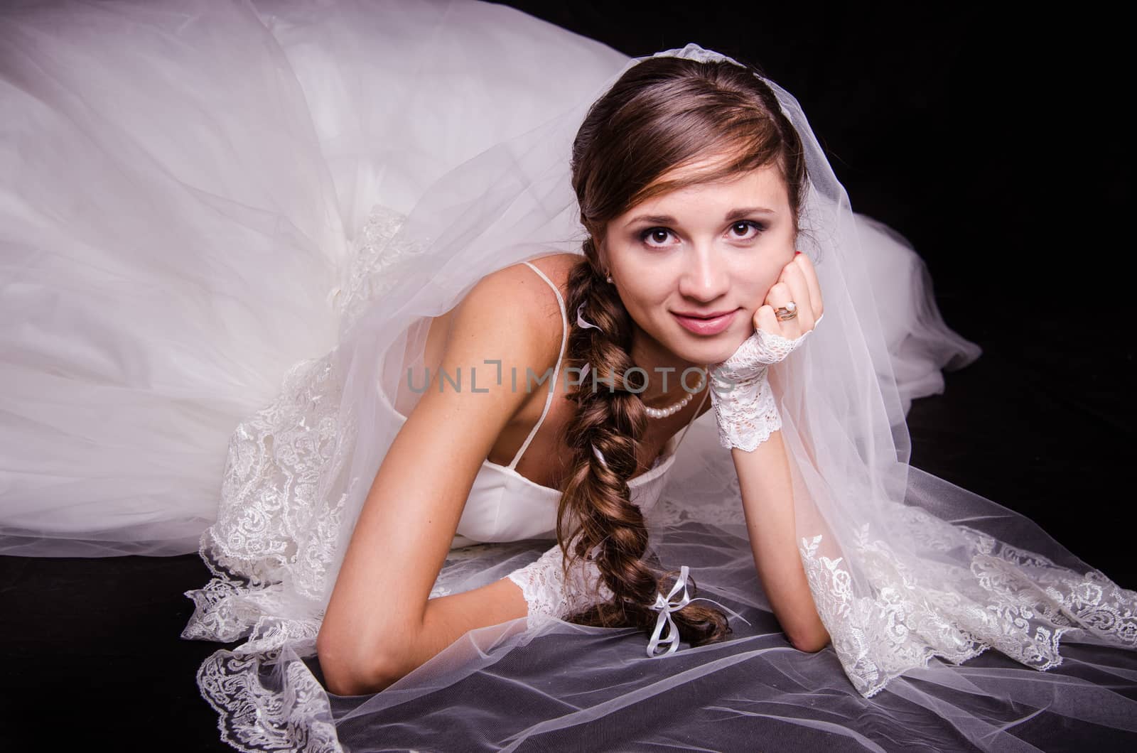 Portrait of the bride of the European type, lying on a black background in a wedding dress
