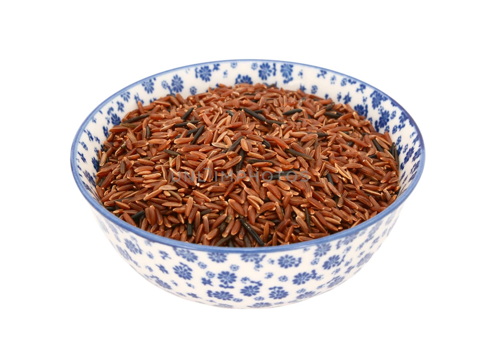 Camargue red rice grains in a blue and white porcelain bowl with a floral design, isolated on a white background
