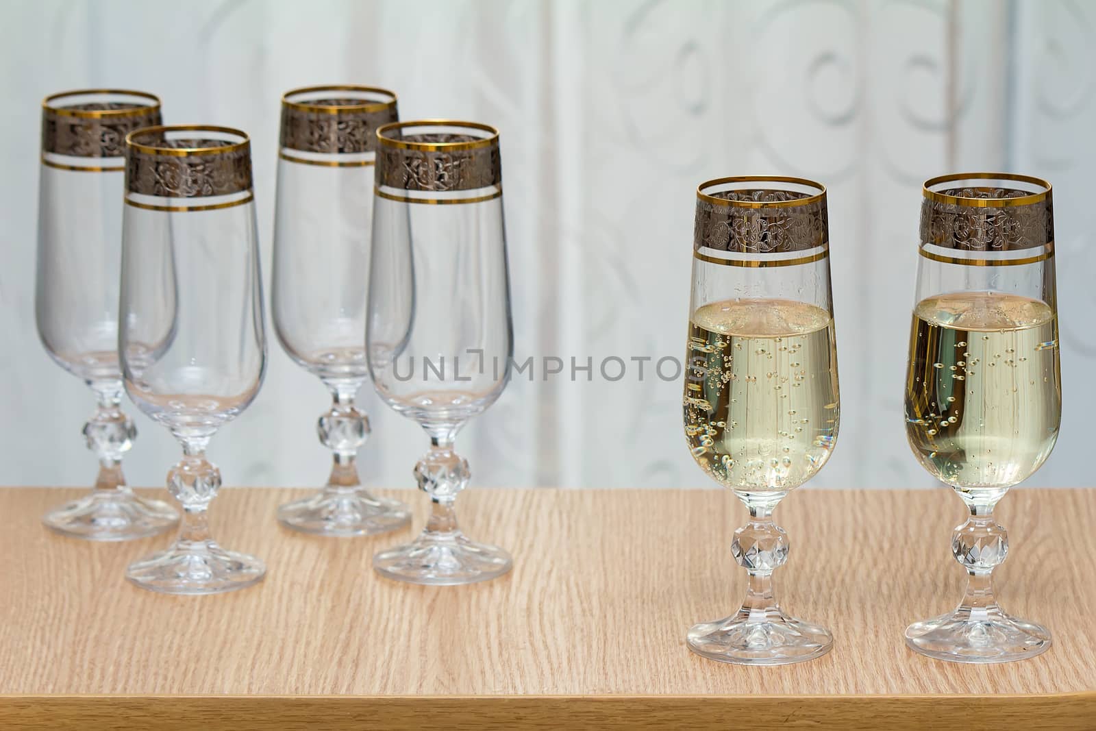On the table near the window there are six beautiful glass , two filled with champagne.