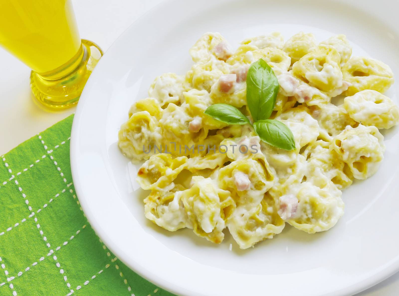 Delicious stuffed pasta tortellini with cream, ham and basil on white dish. Traditional mediterranean cuisine.