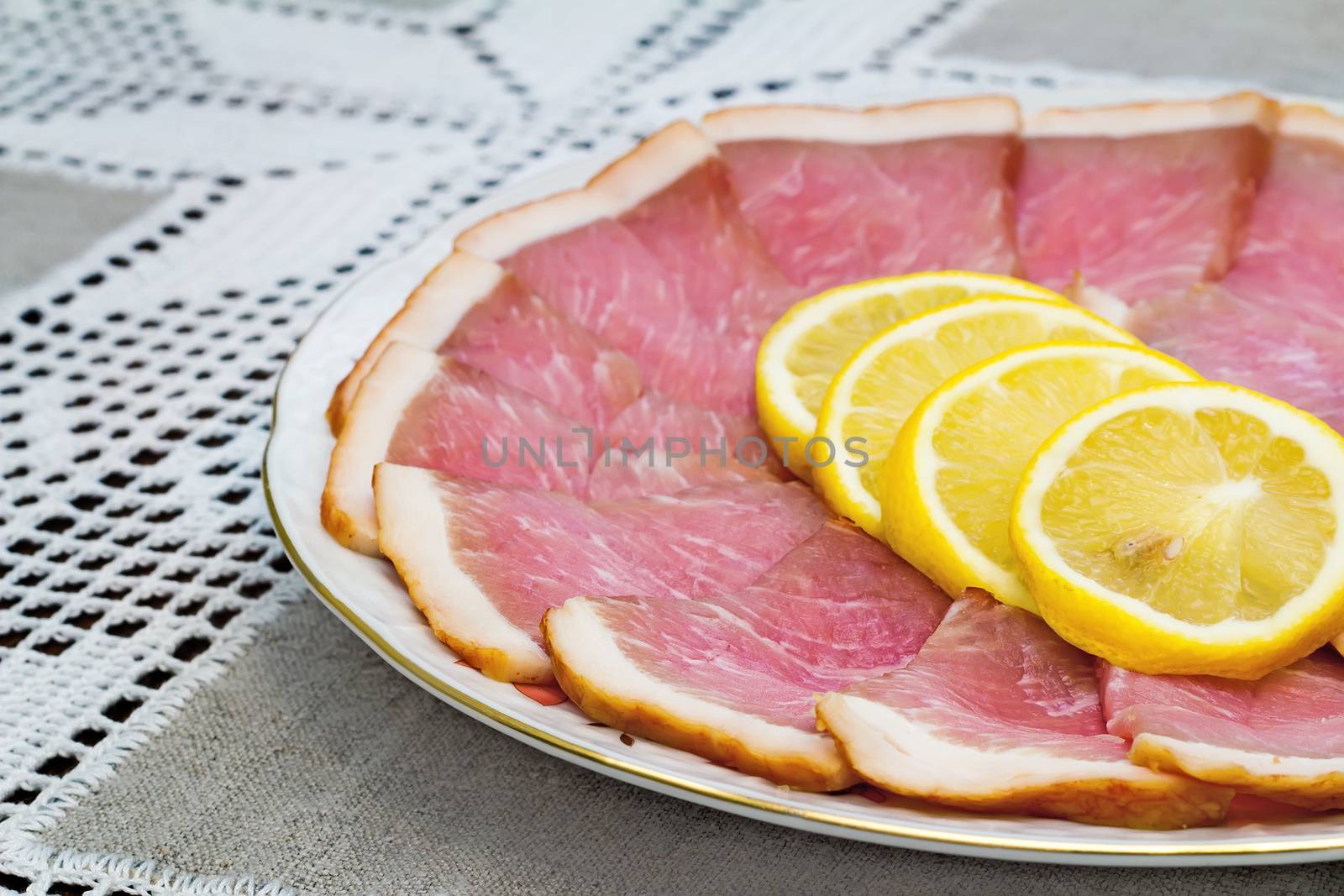 Delicious slices of ham and lemon on the plate, next Cutlery: knife and fork.