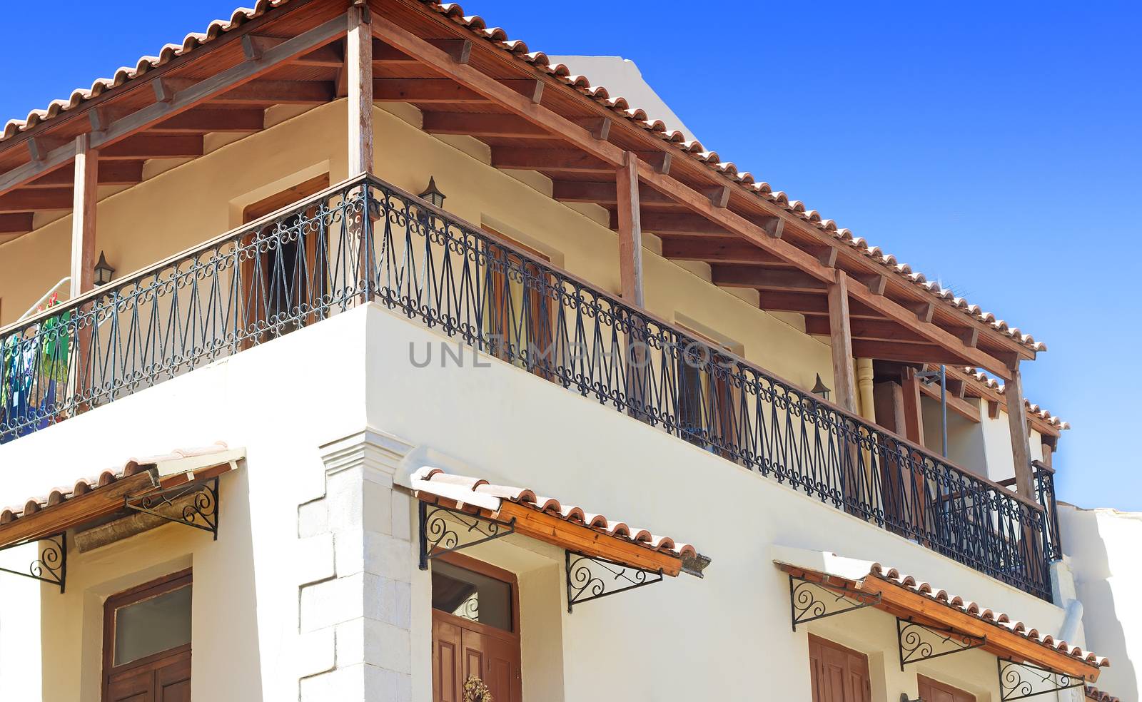 Detail of the facade of an old house on the coast of the island of Crete with a long balcony, fenced wrought metal fence.