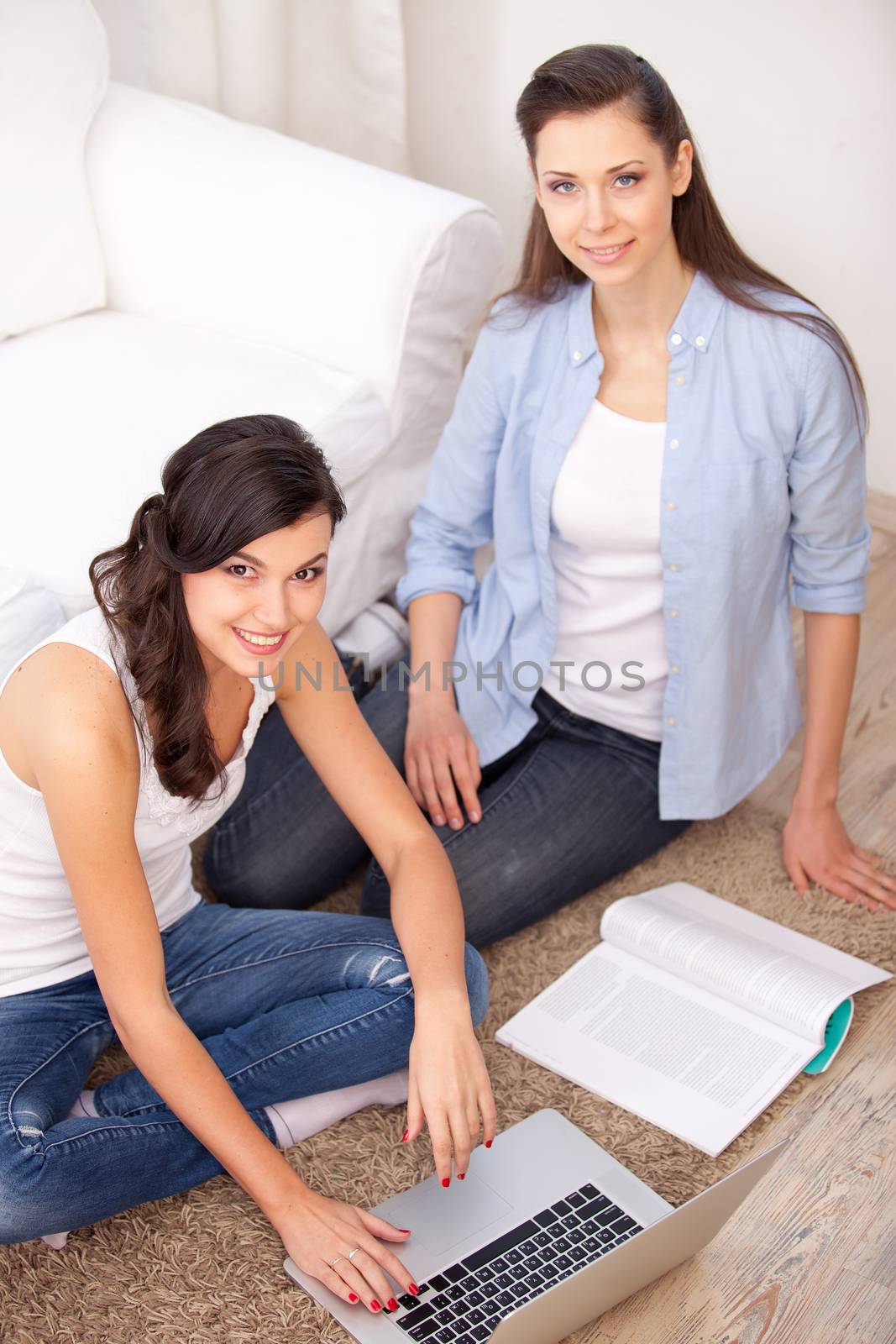 two young  women resting with notebook on floor near sofa, at campus