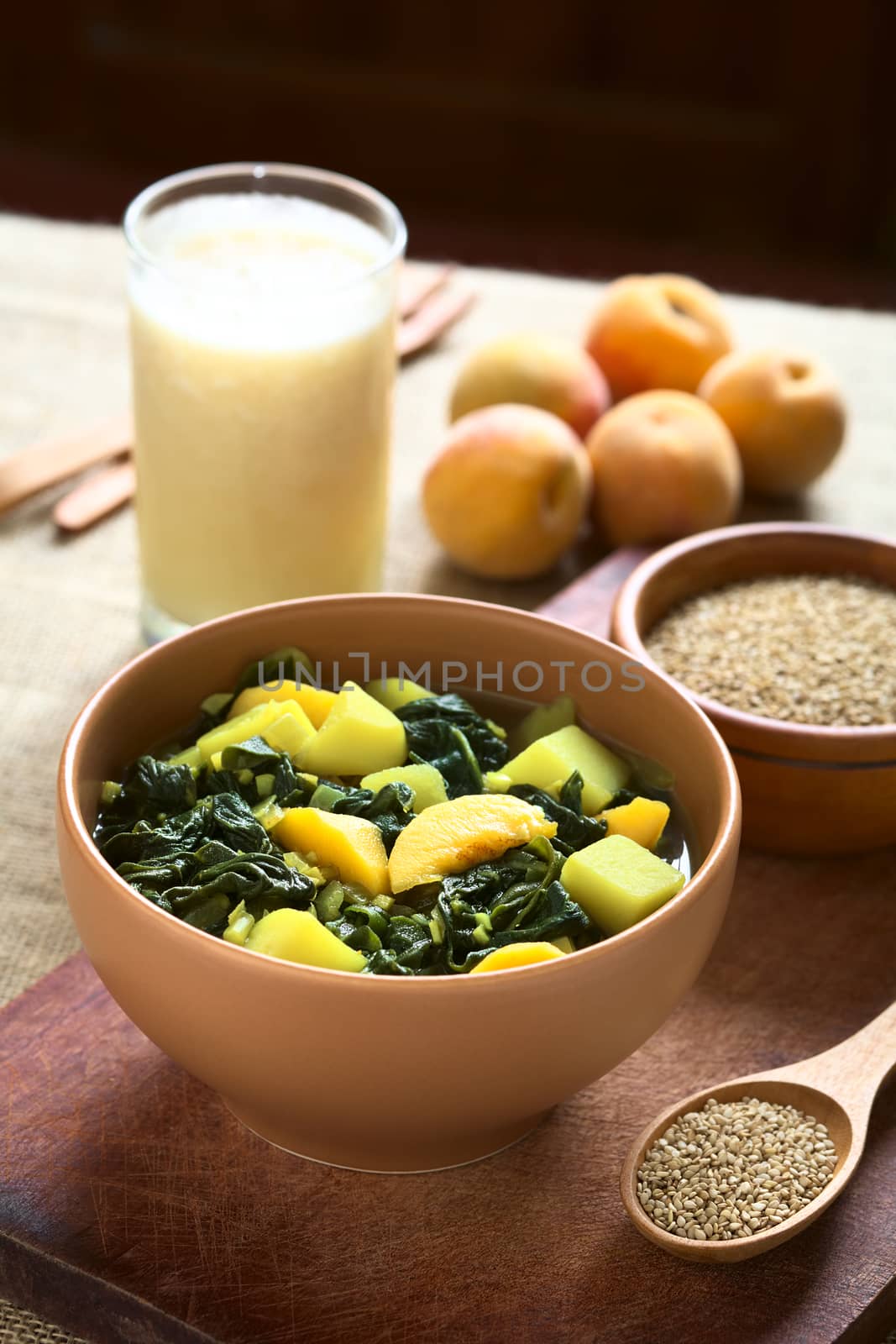 Bowl of spinach, peach and potato curry dish with sesame seeds, peaches and lassi in the back photographed with natural light (Selective Focus, Focus one third into the curry dish)