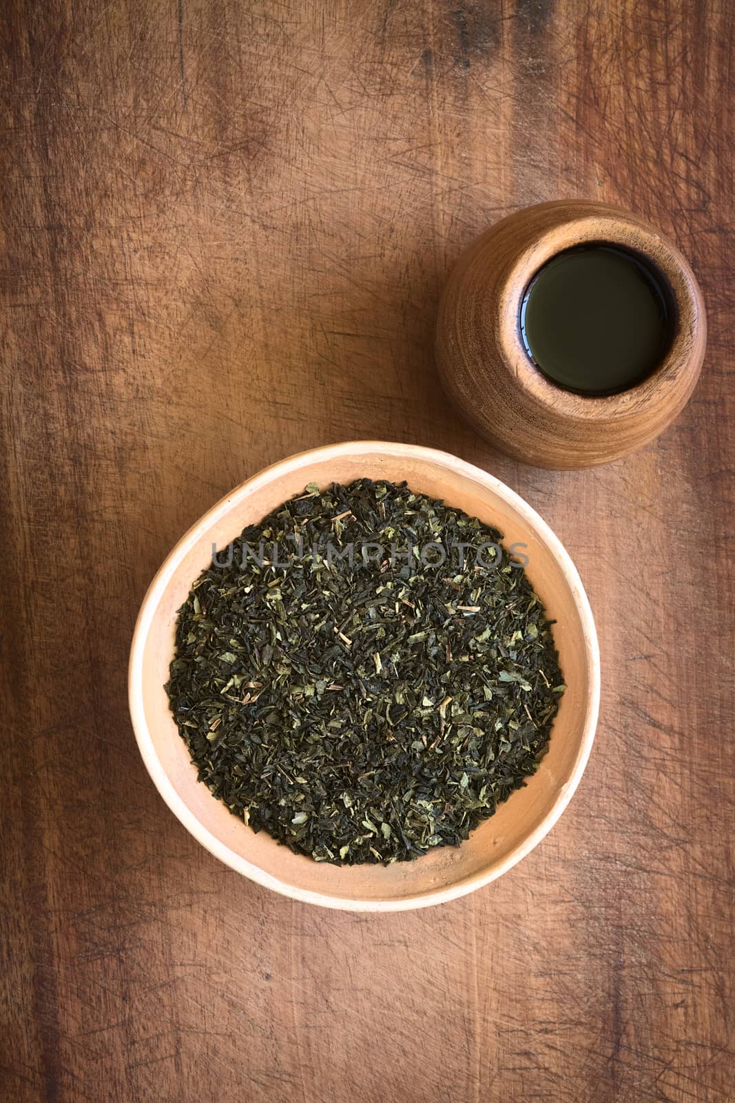 Overhead shot of dried green tea leaves in bowl with tea in wooden cup on wood photographed with natural light