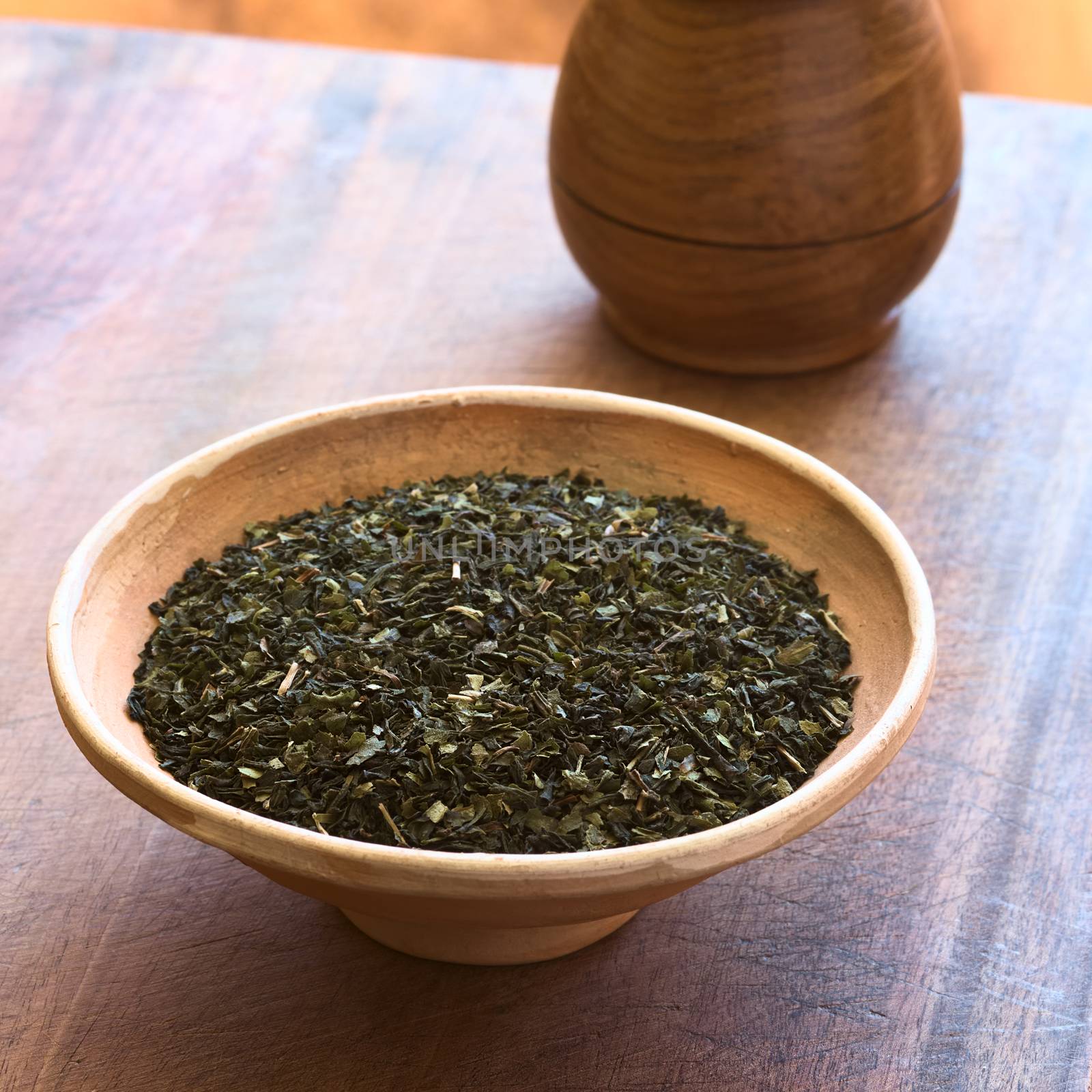 Dried green tea leaves in bowl with tea in wooden cup on wood photographed with natural light (Selective Focus, Focus one third into the tea leaves)