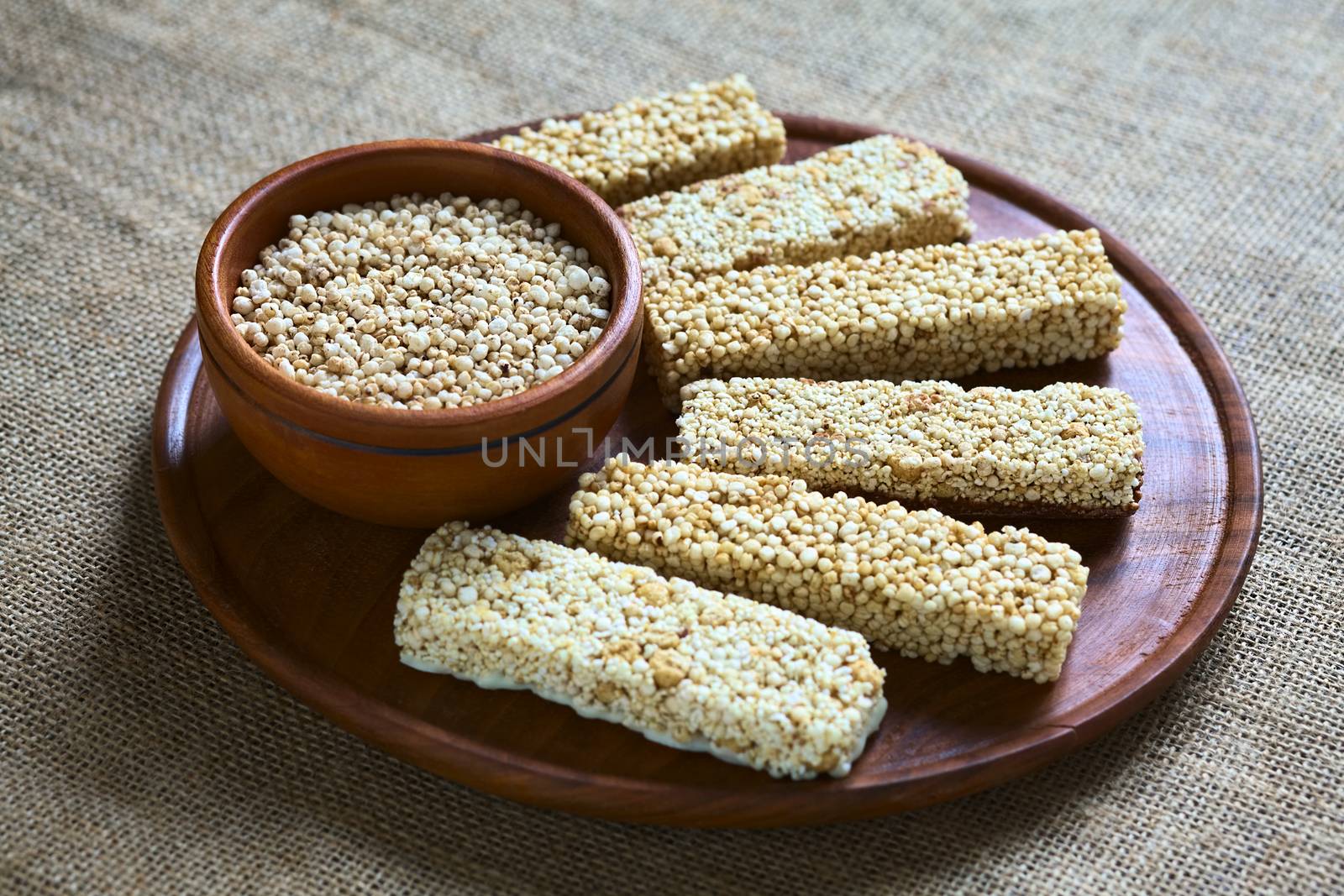 Popped quinoa seeds in bowl with quinoa cereal bars, one with honey the other mixed with amaranth, on wooden plate photographed with natural light (Selective Focus, Focus into the middle of the popped quinoa seeds)