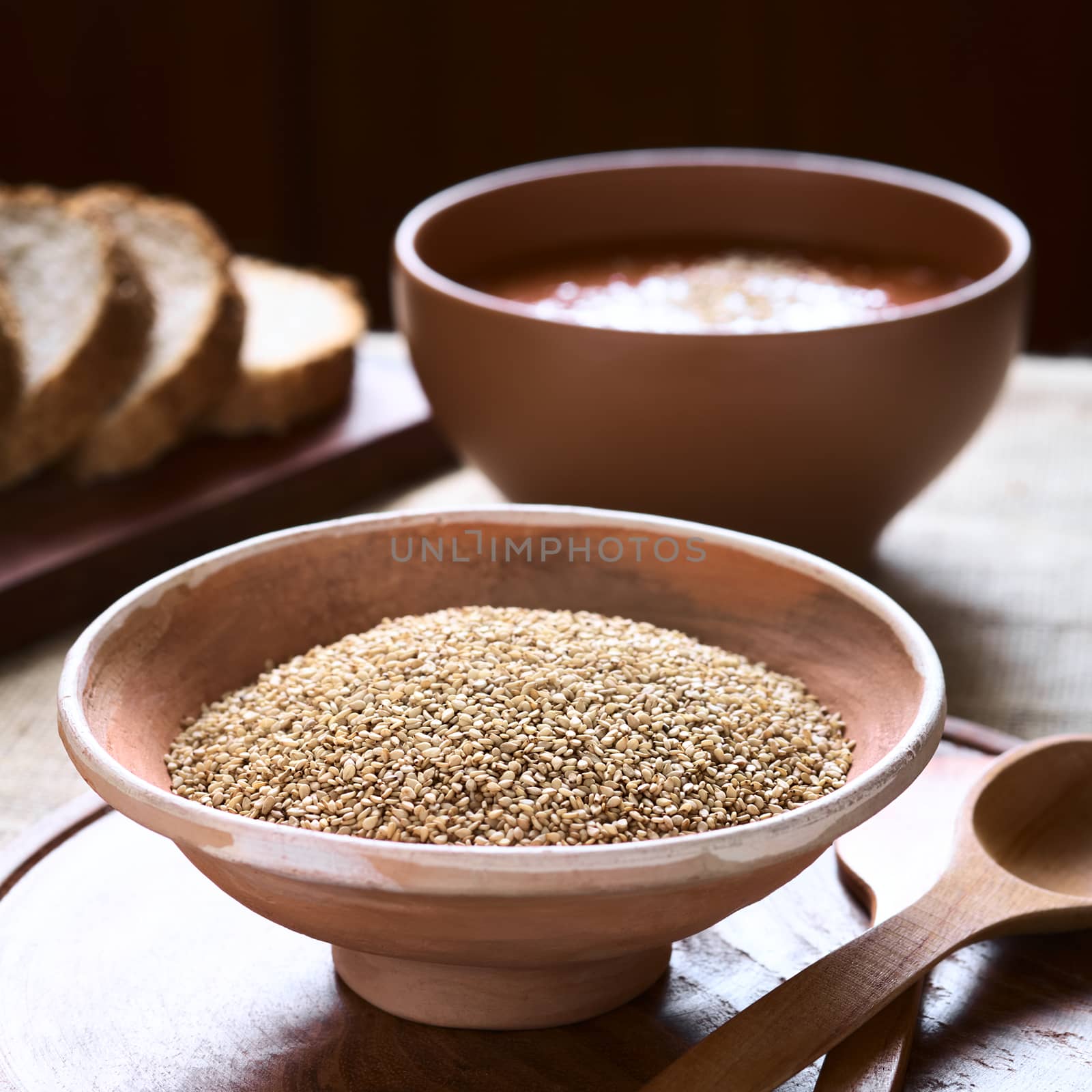 Sesame seeds in bowl with vegetable cream soup and wholegrain bread in the back photographed with natural light (Selective Focus, Focus one third into the seeds)