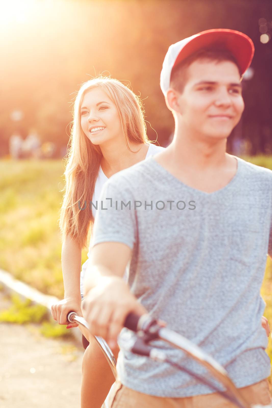 Happy couple - young man and woman riding a bicycle in the park outdoors