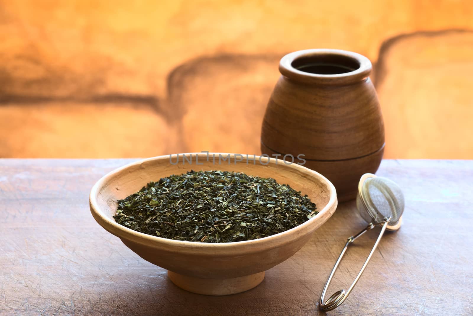 Dried green tea leaves in bowl with a tea strainer and wooden tea cup photographed with natural light (Selective Focus, Focus one third into the tea leaves)  