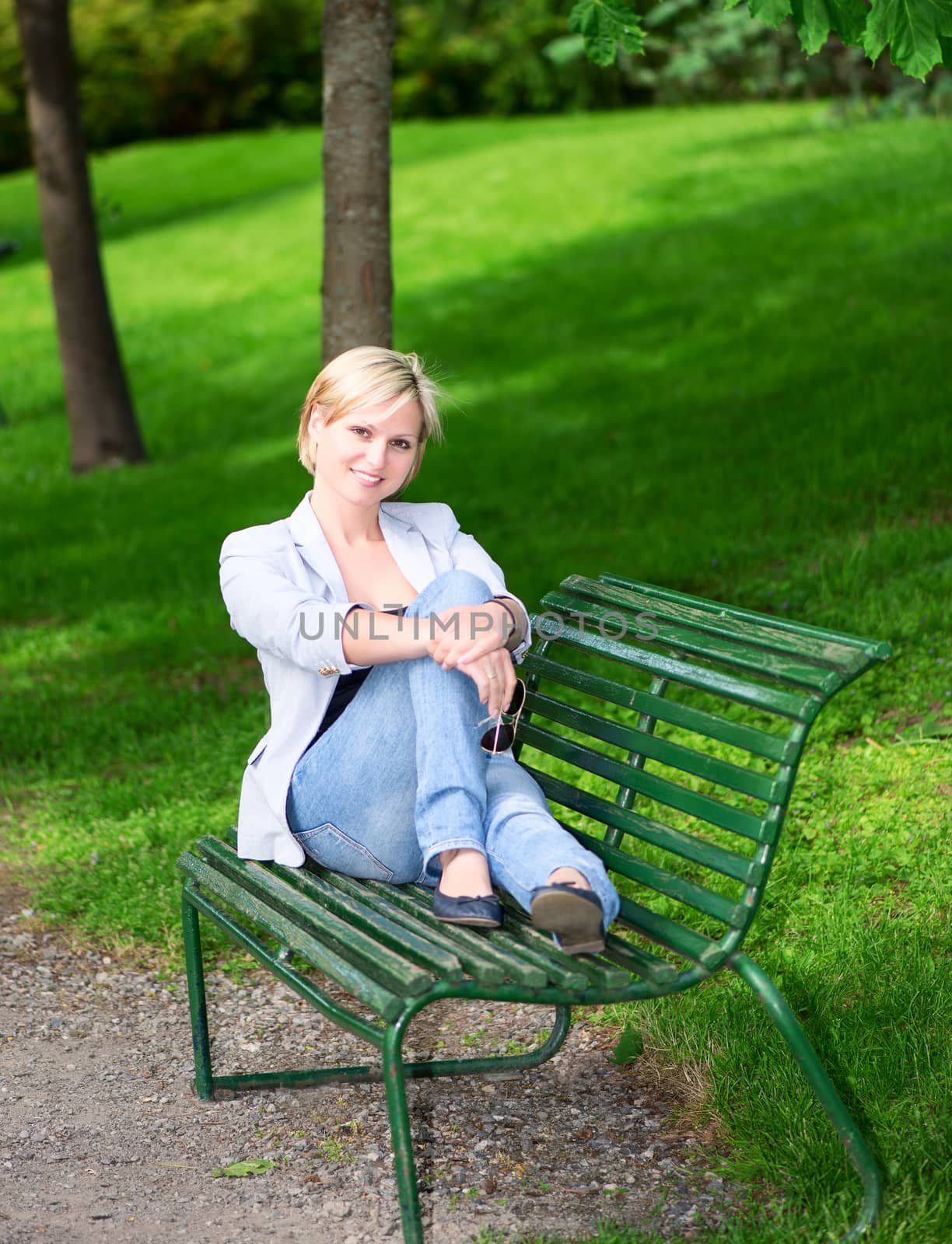young woman sitting on bench in park smiling and looking into the camera
