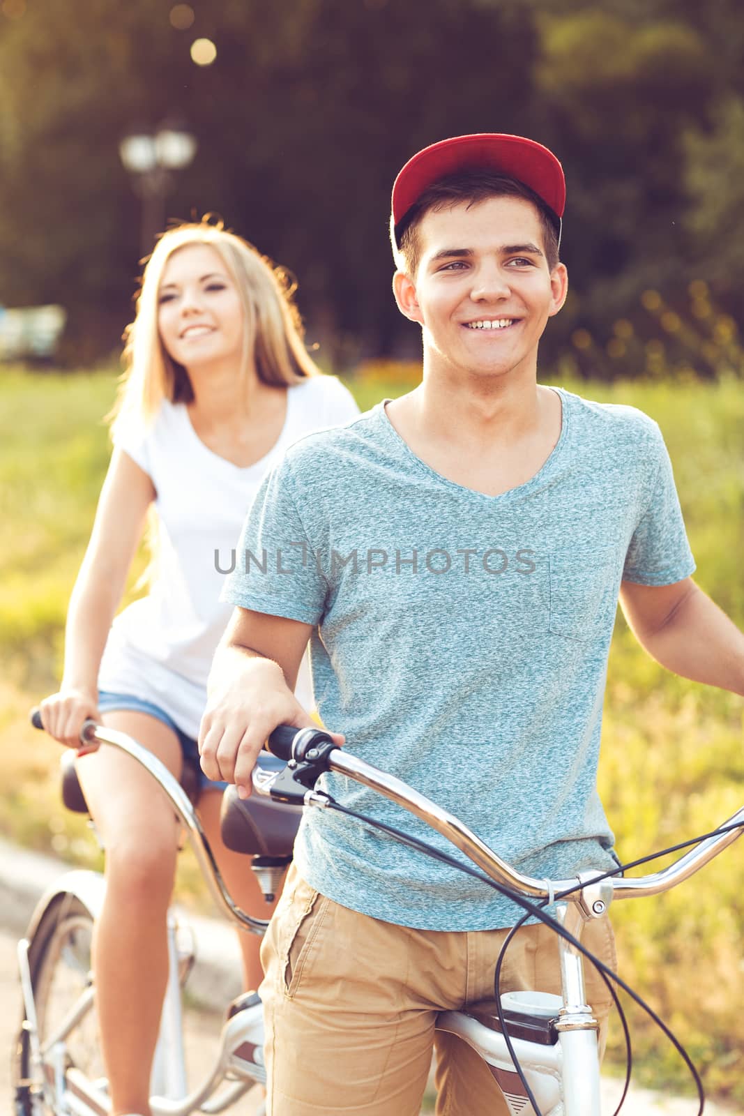 Happy couple - young man and woman riding a bicycle in the park outdoors